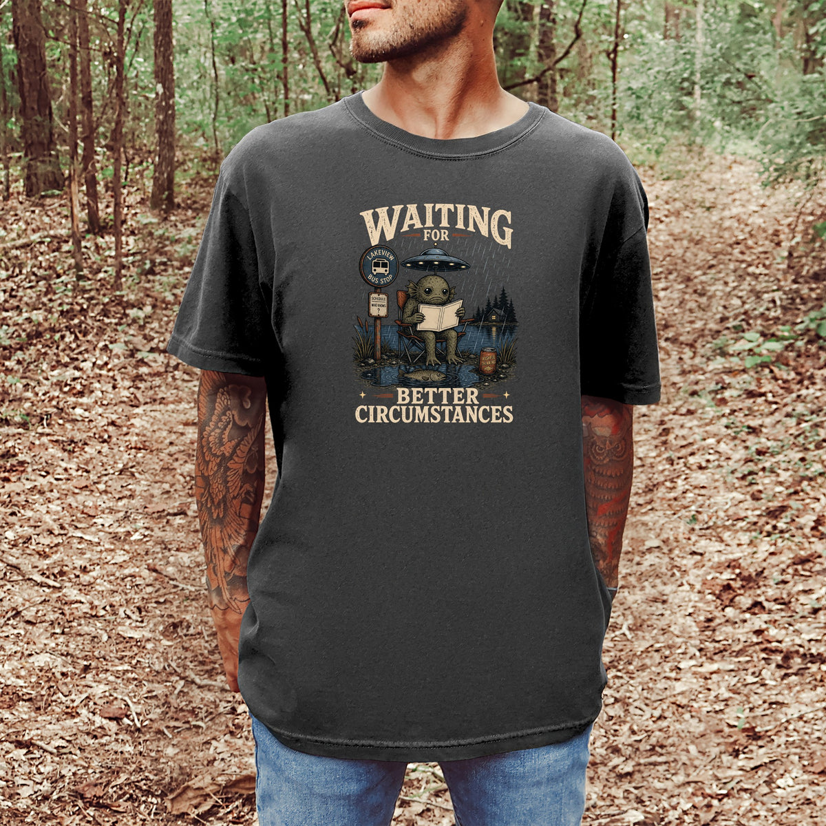 T-shirt graphic of a creature at a bus stop with UFO and text "Waiting for Better Circumstances."