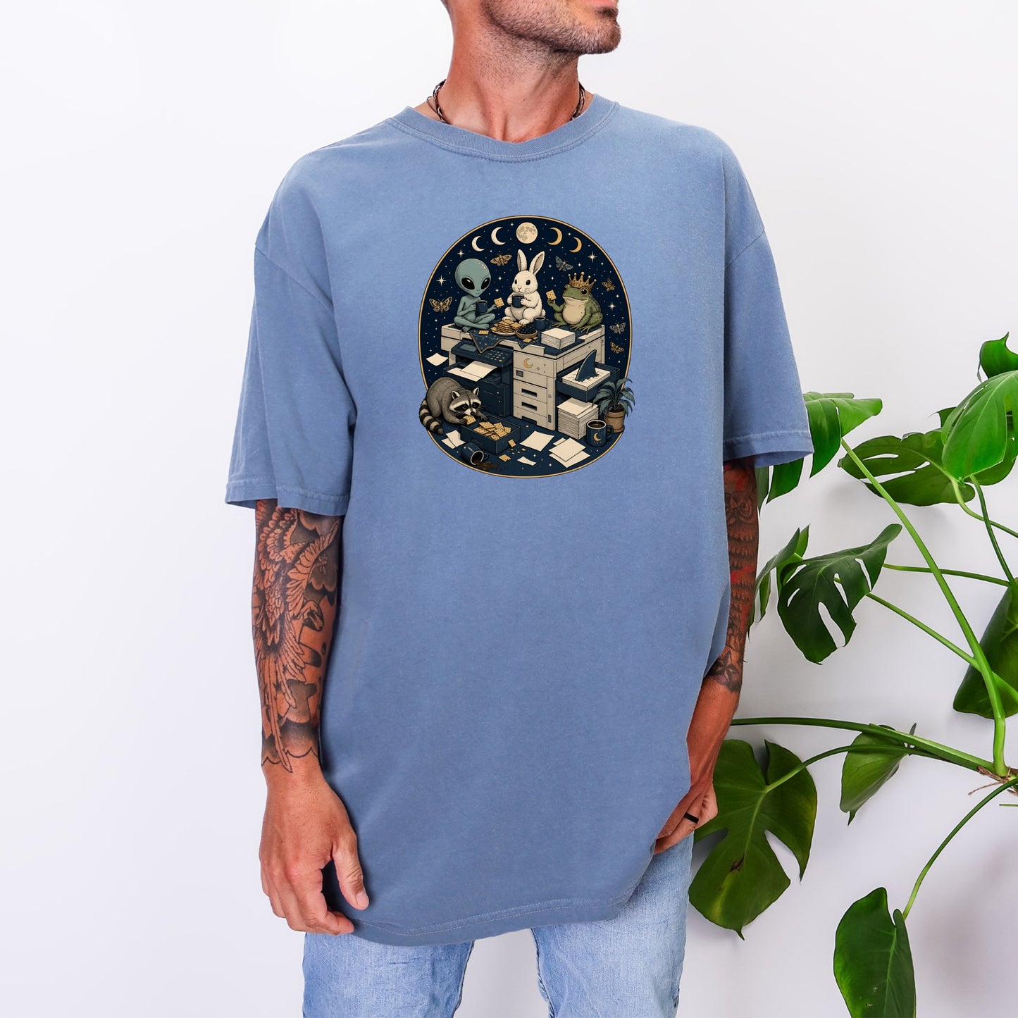 A man wearing an oversized blue t-shirt featuring a graphic of animals around a copy machine.