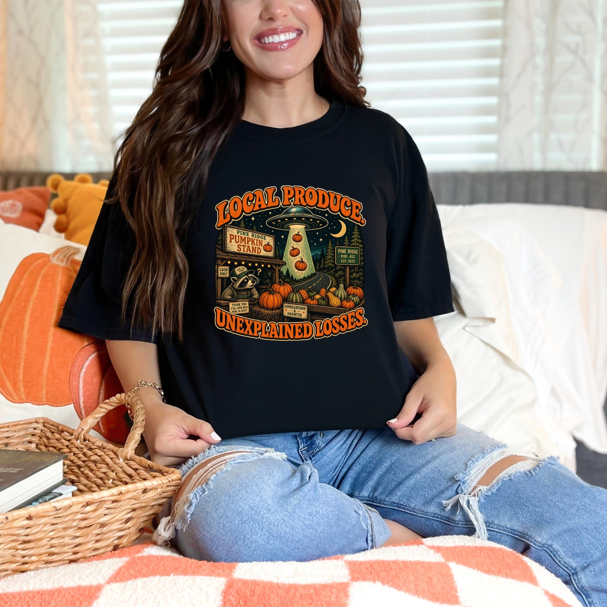 Black t-shirt graphic of a raccoon at a pumpkin stand with a UFO and text "Local Produce Unexplained Losses."