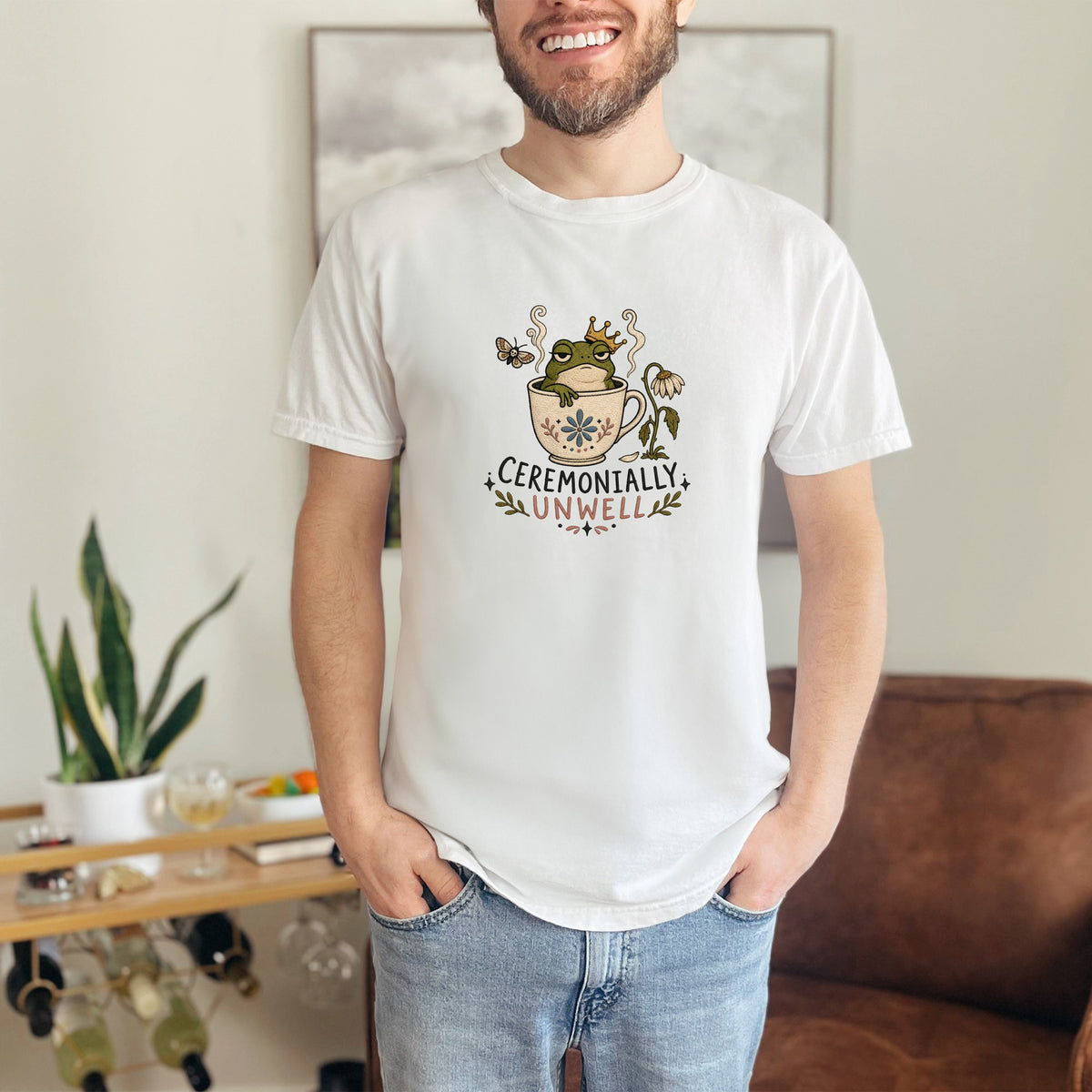 White t-shirt with a frog in a teacup wearing a crown, with text "CEREMONIALY UNWELL".