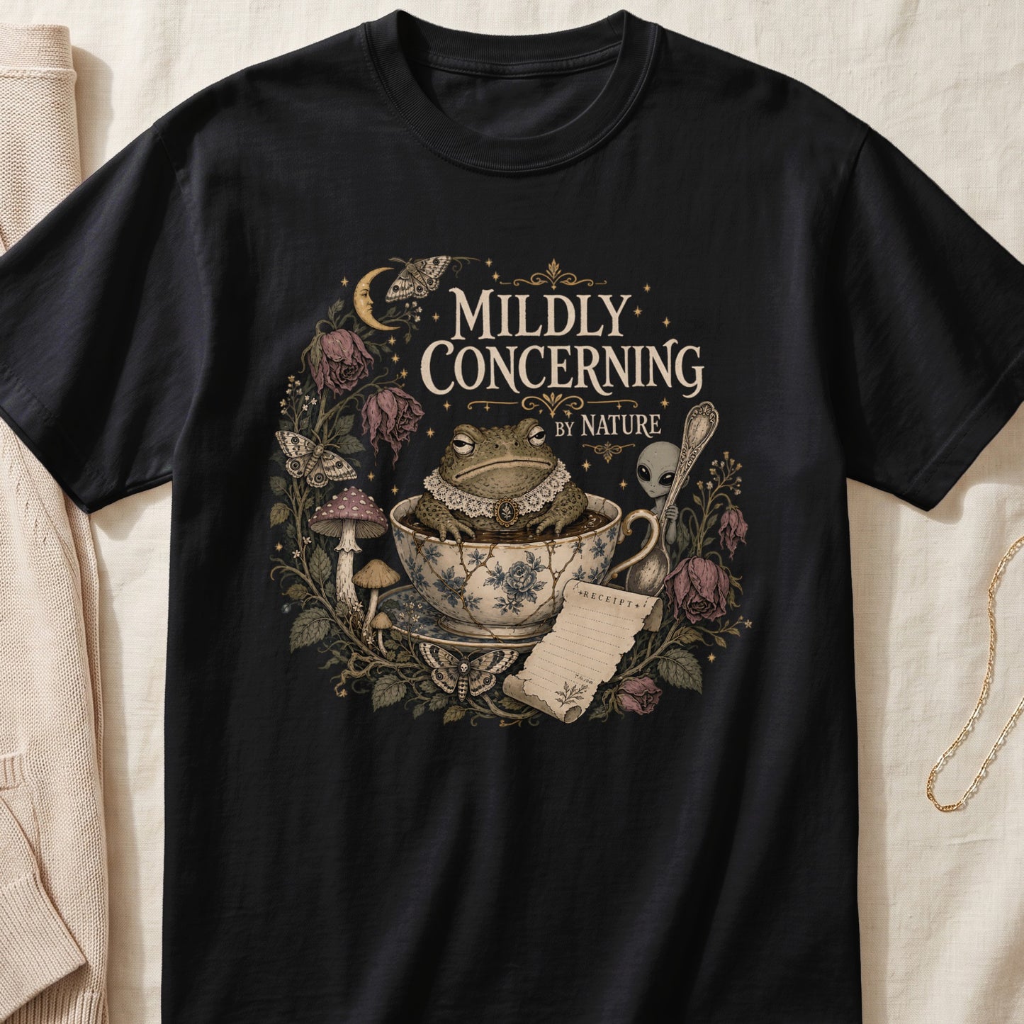 Black t-shirt with "Mildly Concerning By Nature" text, toad, alien, and gothic floral design.