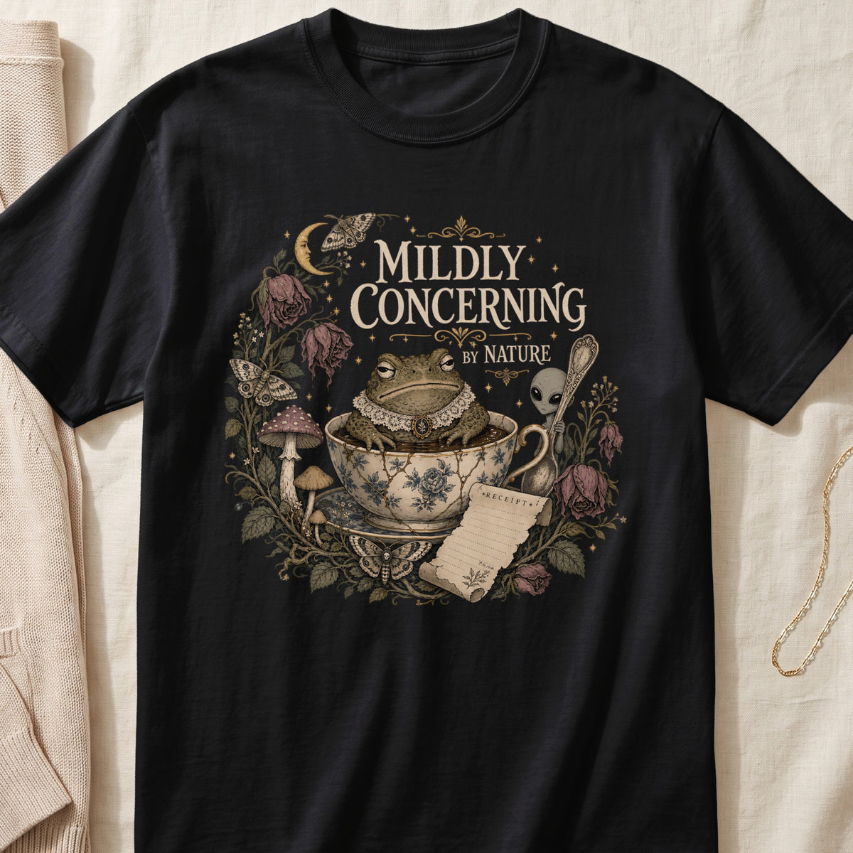 Black t-shirt with "Mildly Concerning By Nature" text, toad, alien, and gothic floral design.