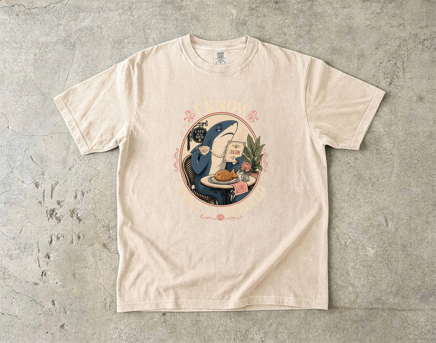 T-shirt graphic of a shark in a pearl necklace holding a menu and cup.