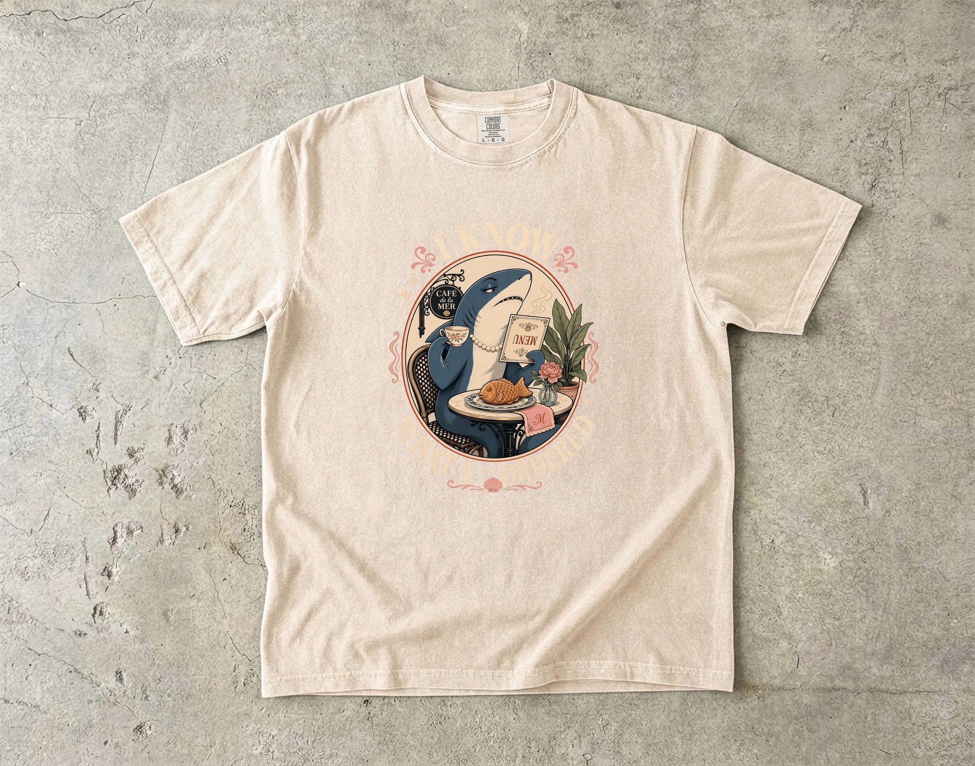 T-shirt graphic of a shark in a pearl necklace holding a menu and cup.