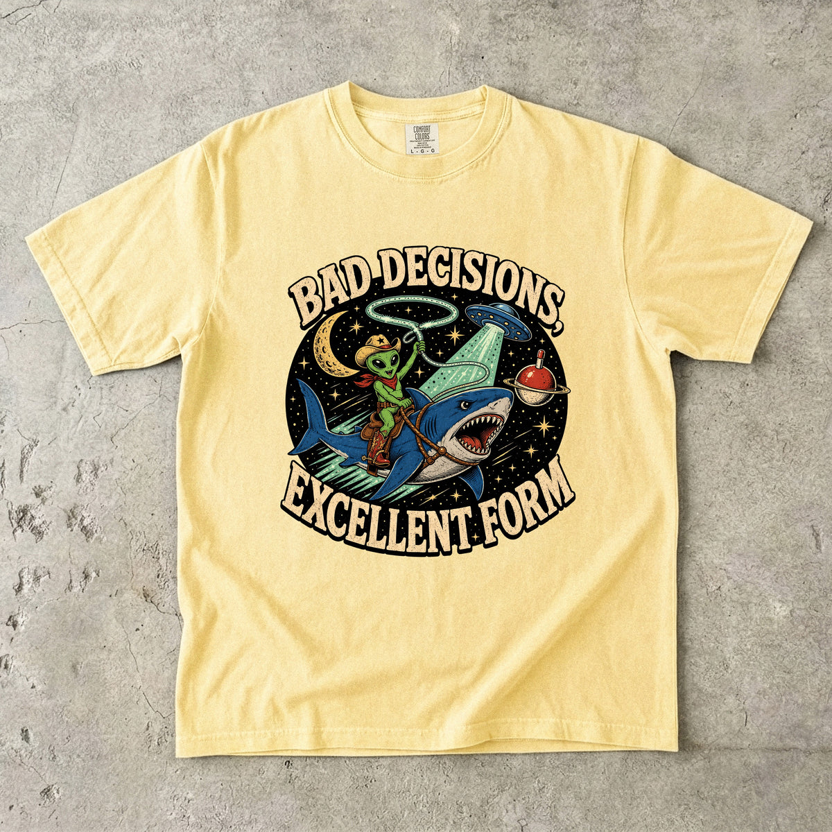 Yellow t-shirt with alien riding shark, UFO, and text "BAD DECISIONS EXCELLENT FORM".