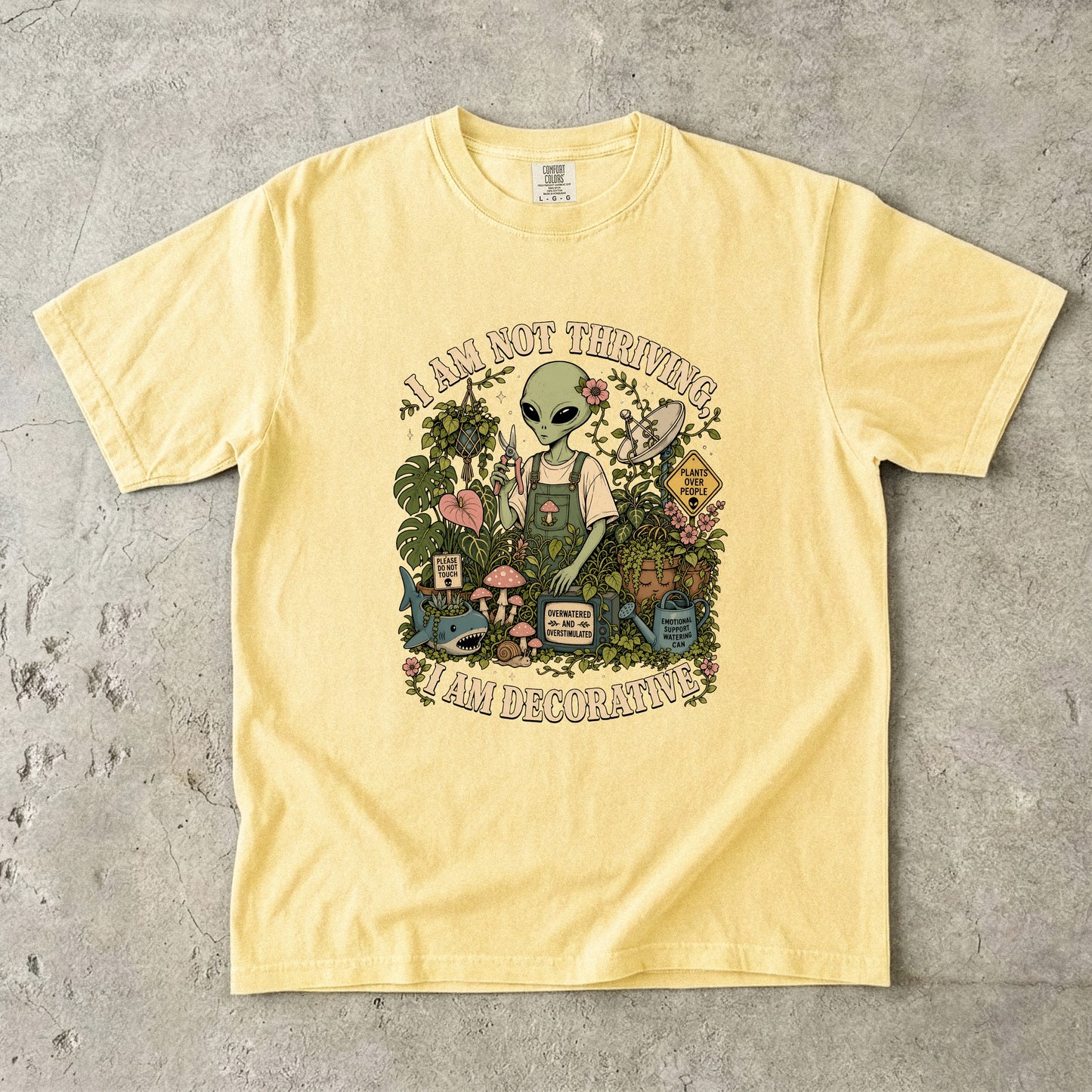 Yellow t-shirt with an alien tending plants, text says "I AM NOT THRIVING, I AM DECORATIVE".