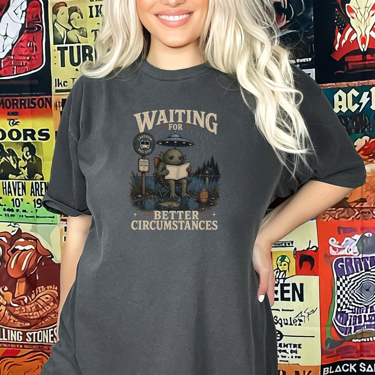 Graphic tee with a creature reading a book under a UFO at a bus stop.