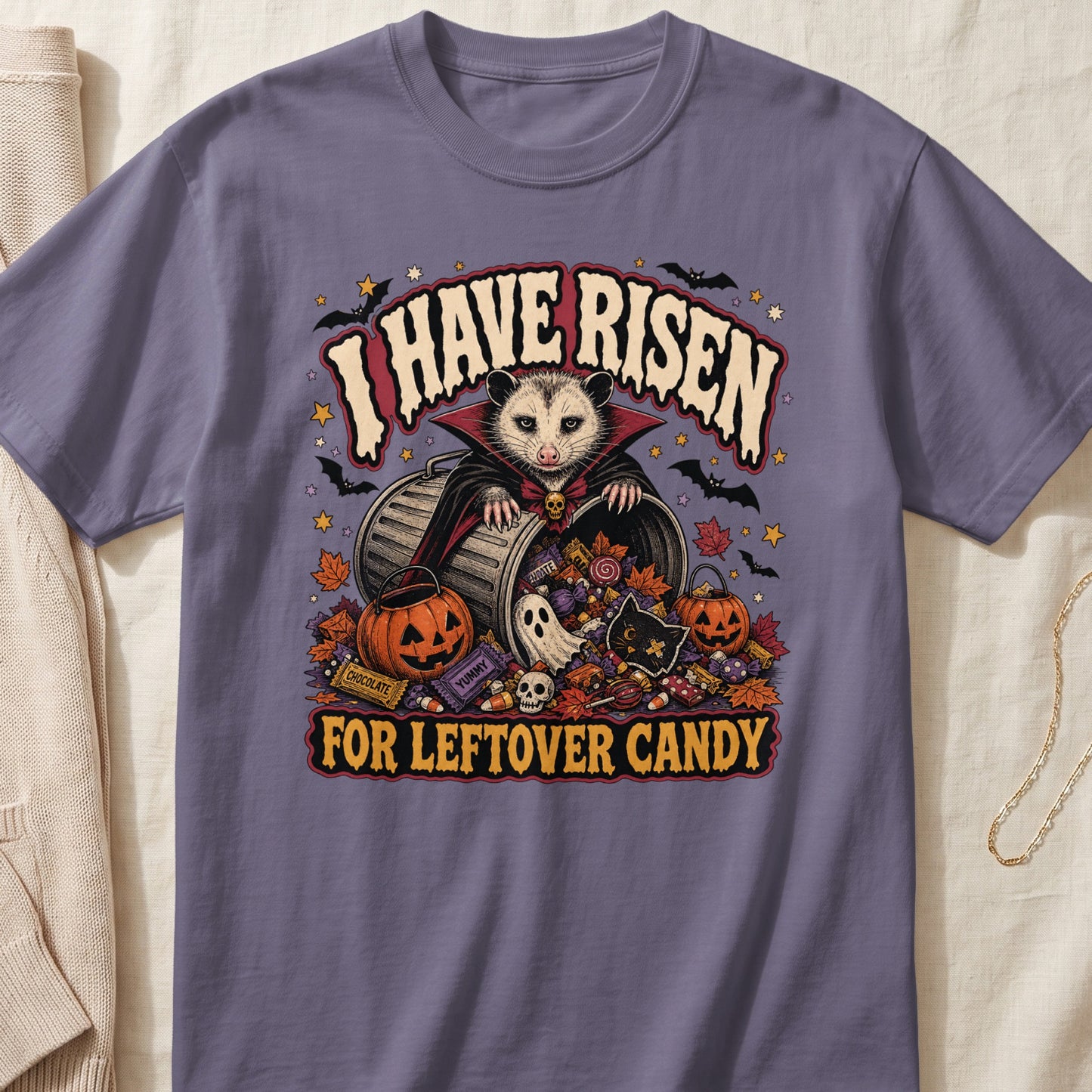 Opossum in a vampire costume sits in a trash can with Halloween candy and decorations.