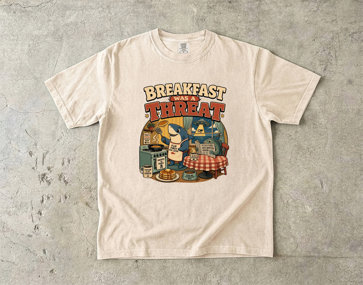 Shirt with a cartoon shark making pancakes, text "BREAKFAST WAS A THREAT".