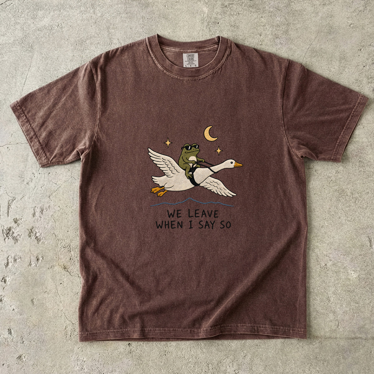 Brown t-shirt with a graphic of a frog riding a goose with the text "WE LEAVE WHEN I SAY SO".