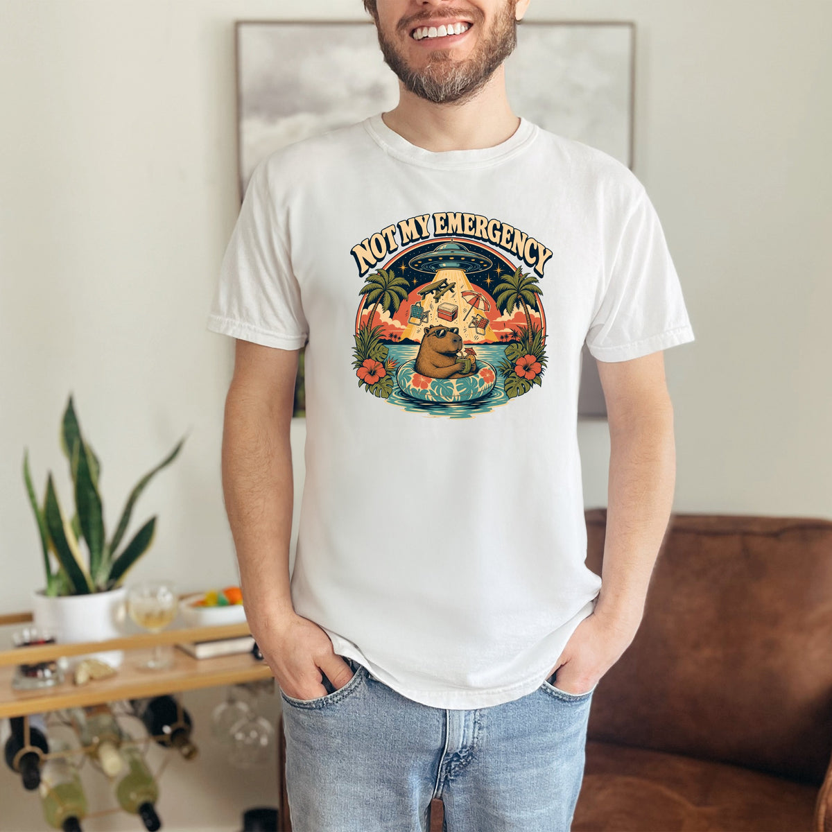 T-shirt graphic with text "NOT MY EMERGENCY" featuring a capybara on a float and a UFO.