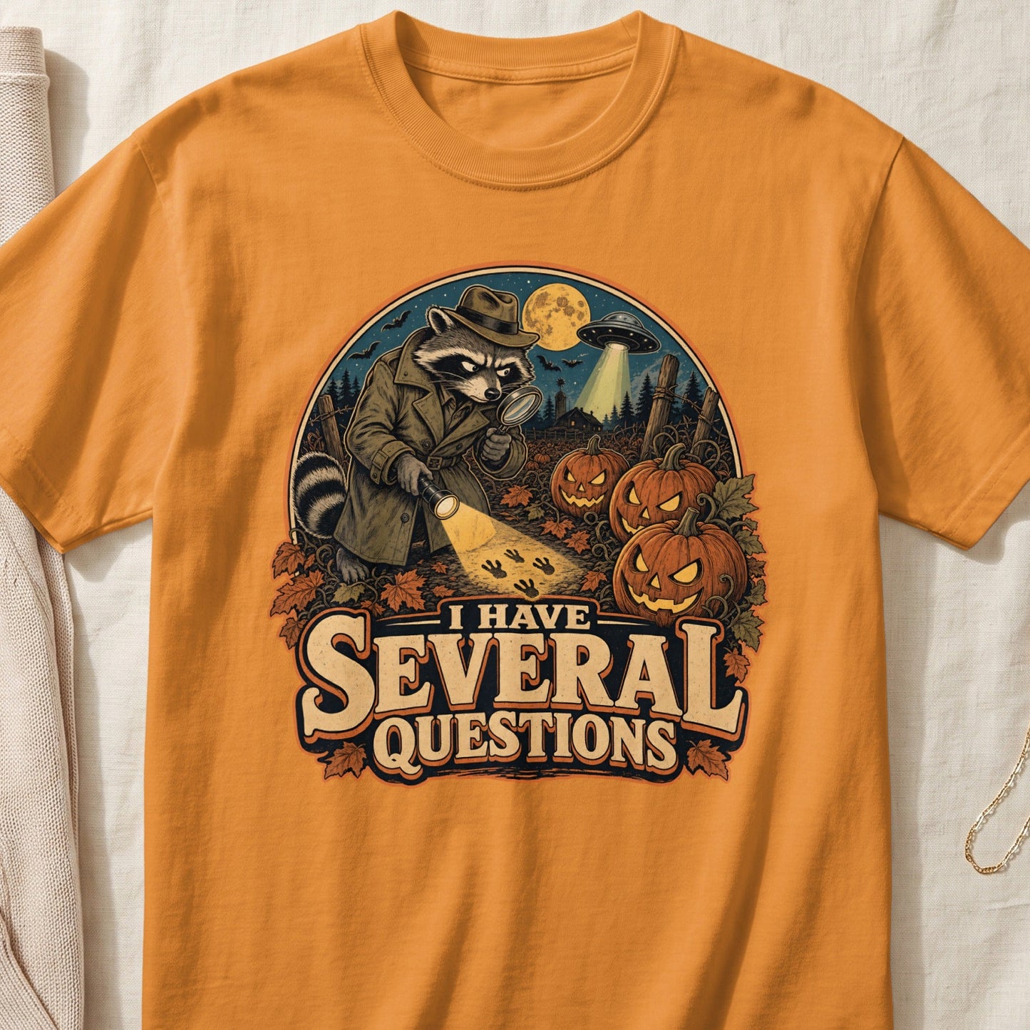Raccoon detective with magnifying glass and flashlight, with pumpkins, UFO, and text "I HAVE SEVERAL QUESTIONS".