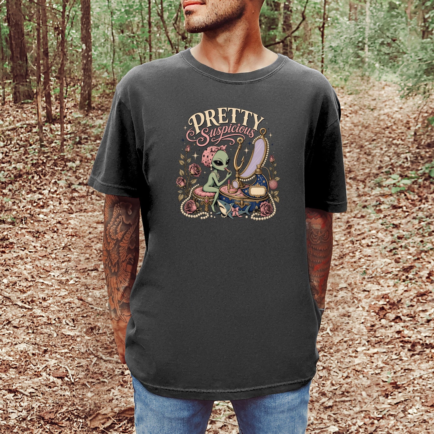 T-shirt graphic with "Pretty Suspicious" text and an alien applying makeup by a mirror.