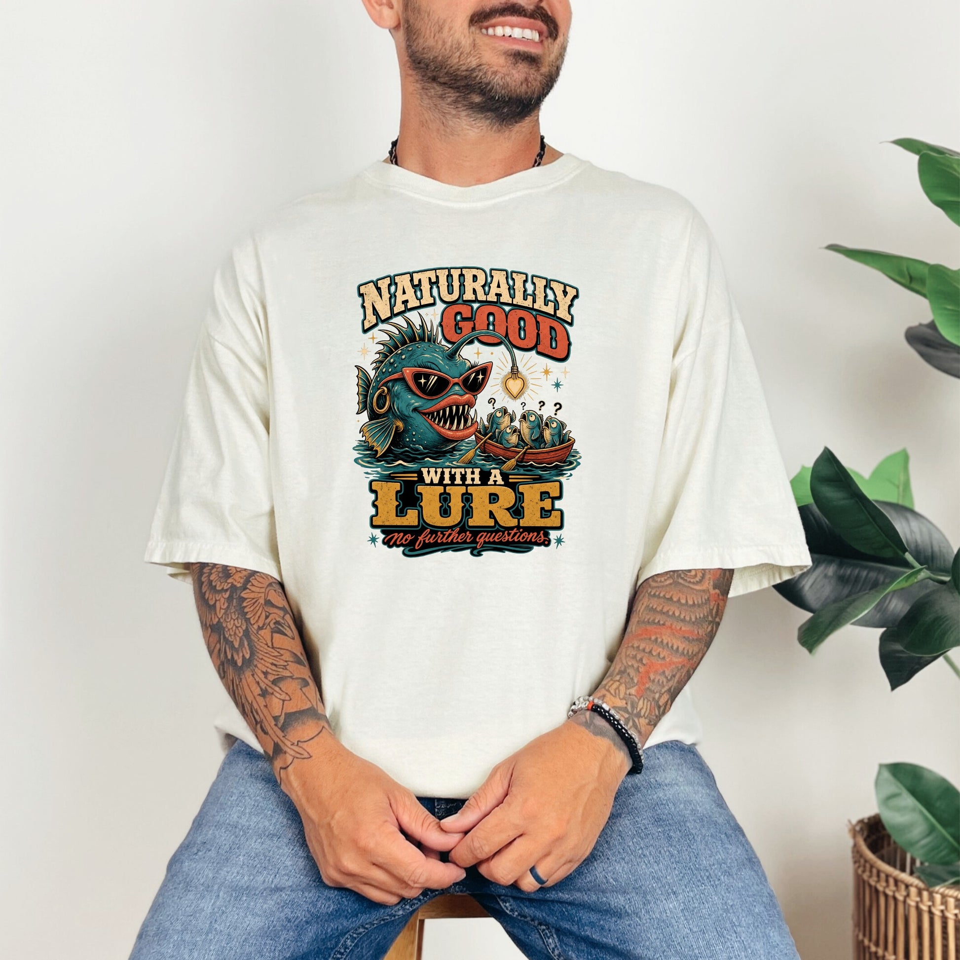 Graphic tee with a cartoon anglerfish, fishing boat, and text "Naturally Good With A Lure".