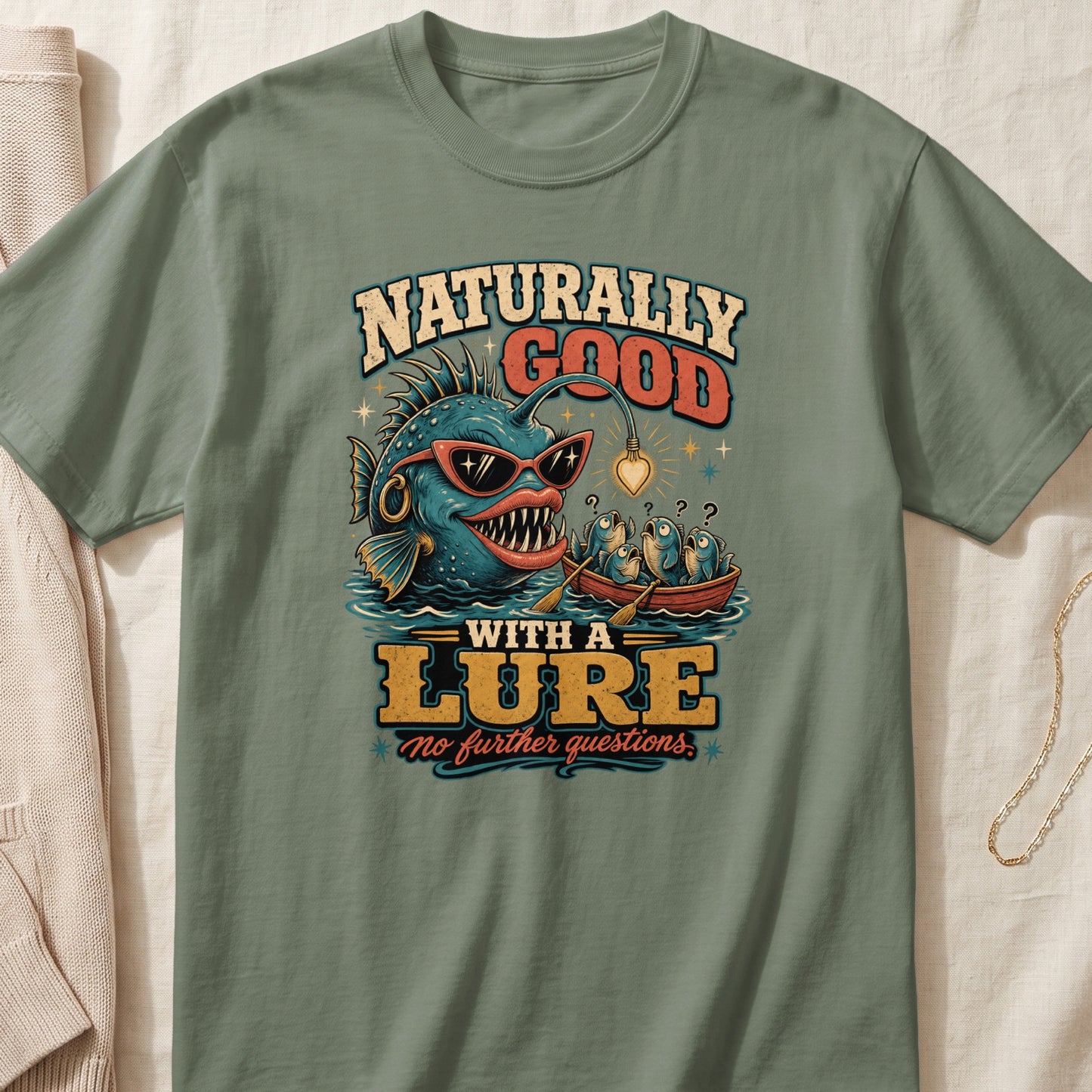 T-shirt graphic with anglerfish and fish in a boat, text says "Naturally Good With A Lure".