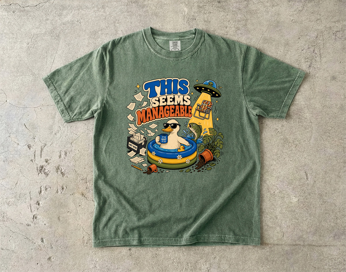 Green t-shirt with "THIS SEEMS MANAGEABLE" graphic featuring a duck in a pool and a UFO.
