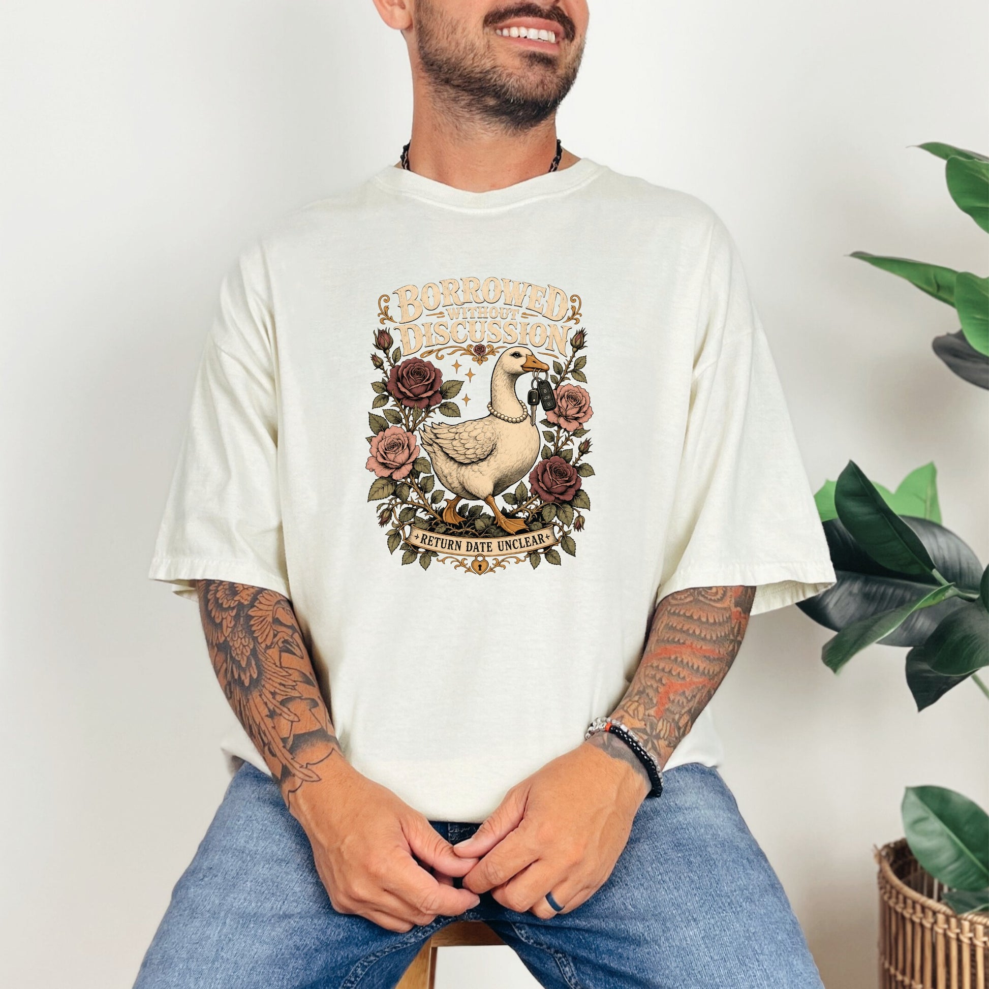 Cream t-shirt with a graphic of a duck holding keys, surrounded by roses and text.