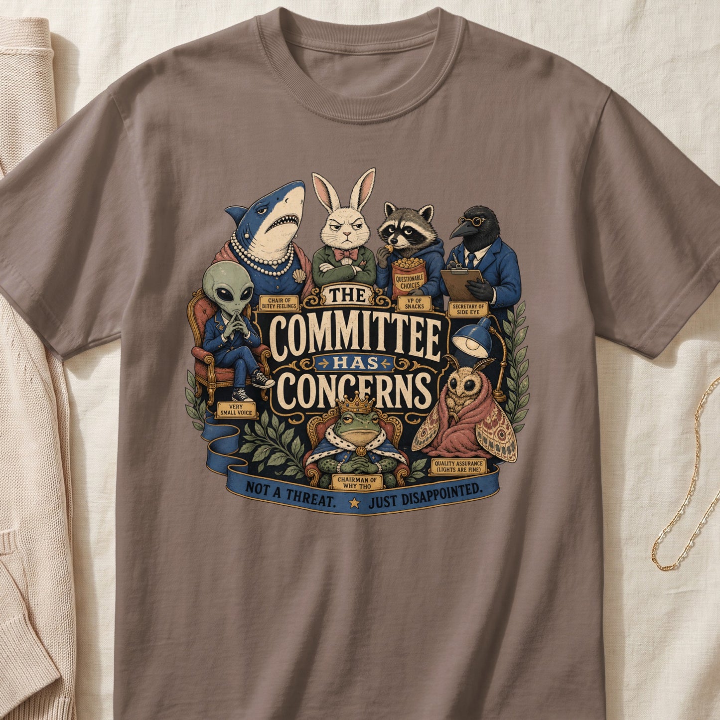 A taupe crewneck t-shirt featuring a cartoon graphic of diverse anthropomorphic animals with the text The Committee Has Concerns.