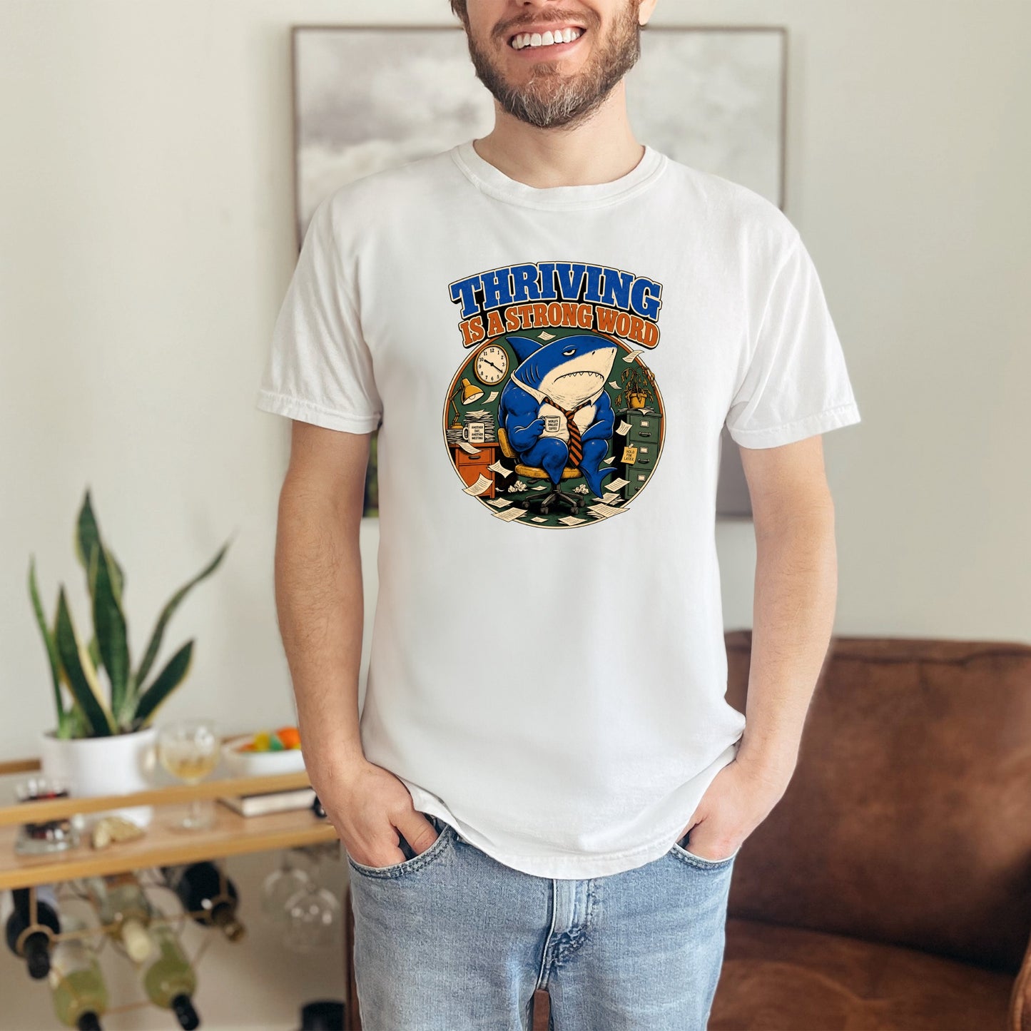 White t-shirt featuring a cartoon shark in a suit with the text "THRIVING IS A STRONG WORD".