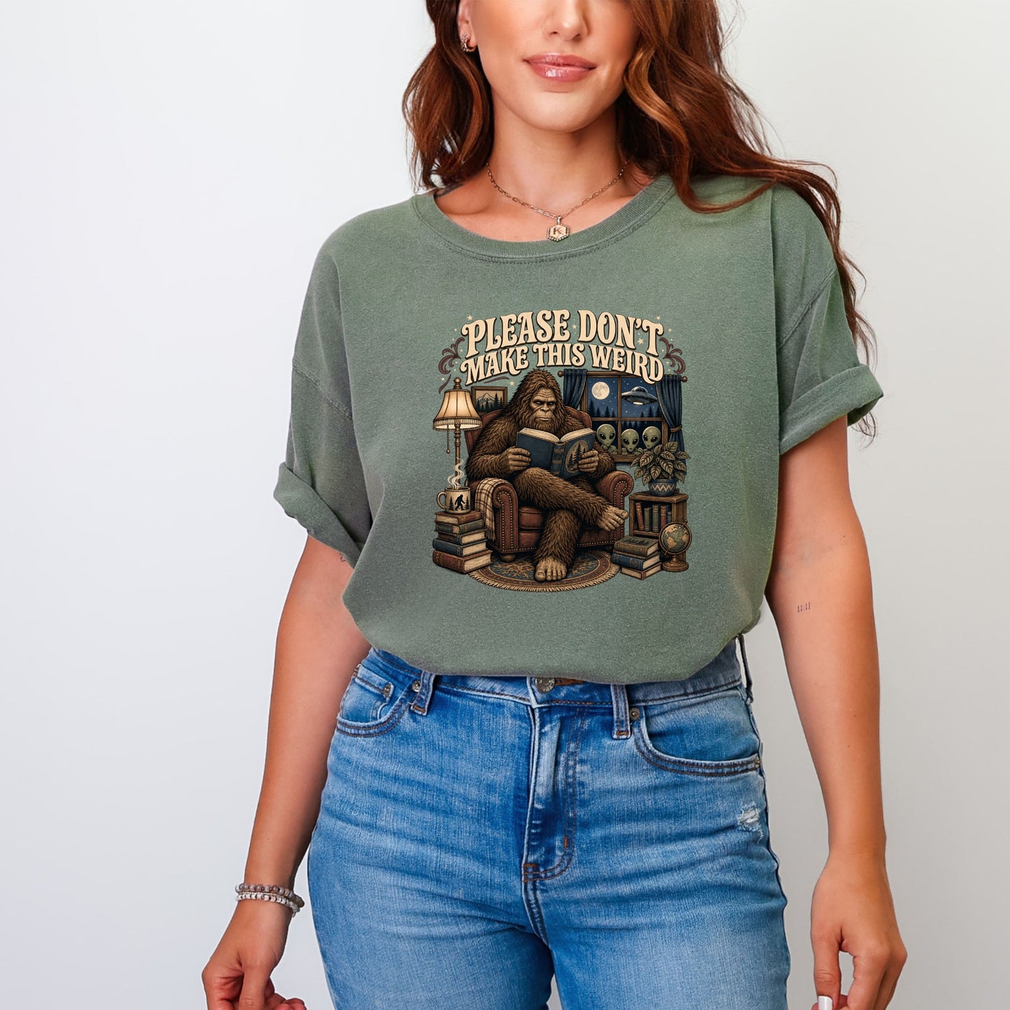 Graphic tee with Bigfoot reading by lamplight with aliens outside window.