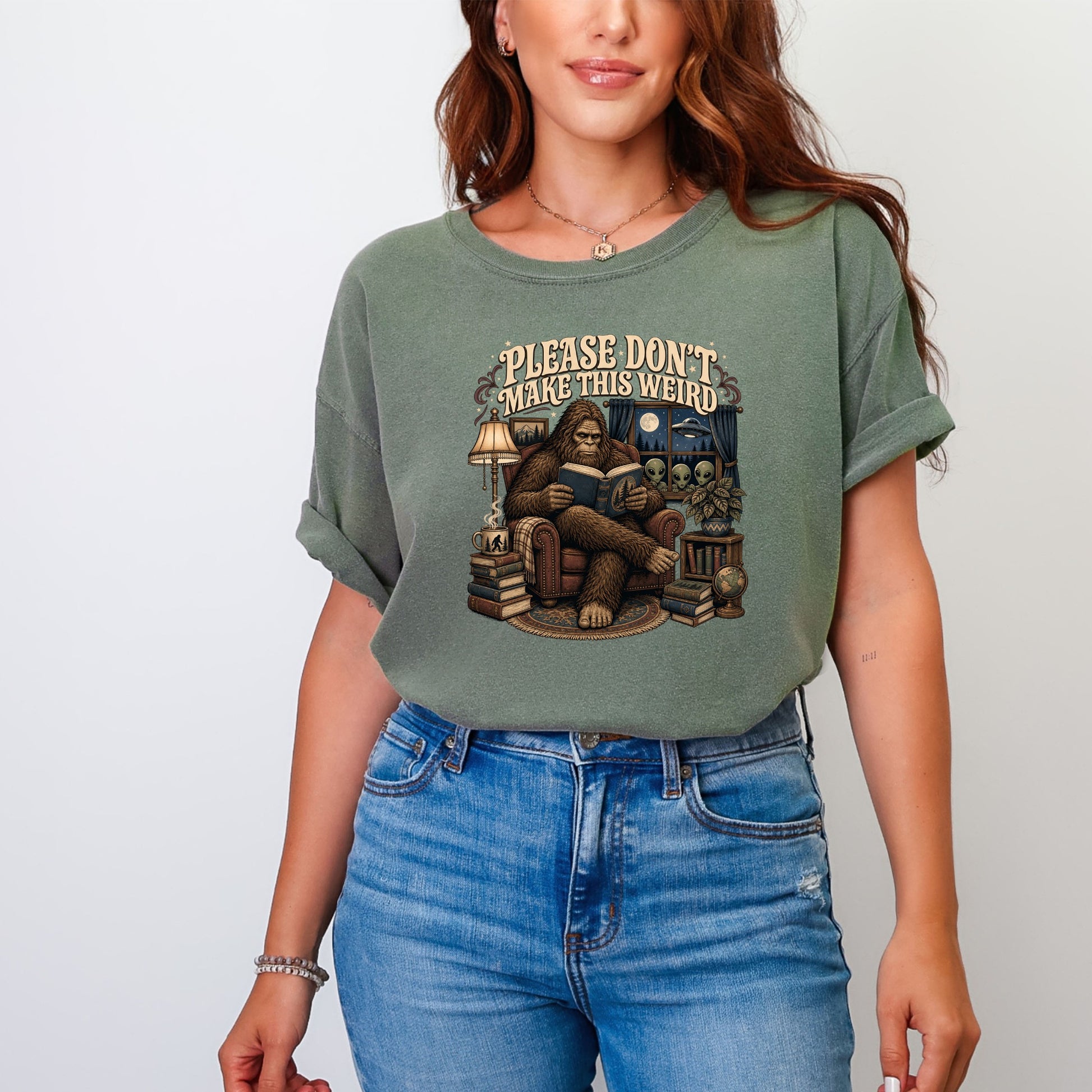Graphic tee with Bigfoot reading by lamplight with aliens outside window.