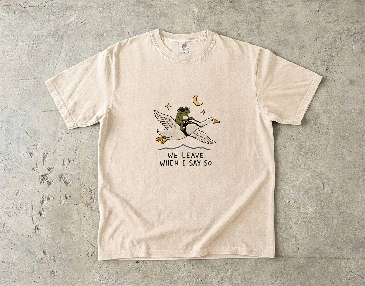 T-shirt with graphic of frog riding goose under moon with text "WE LEAVE WHEN I SAY SO".