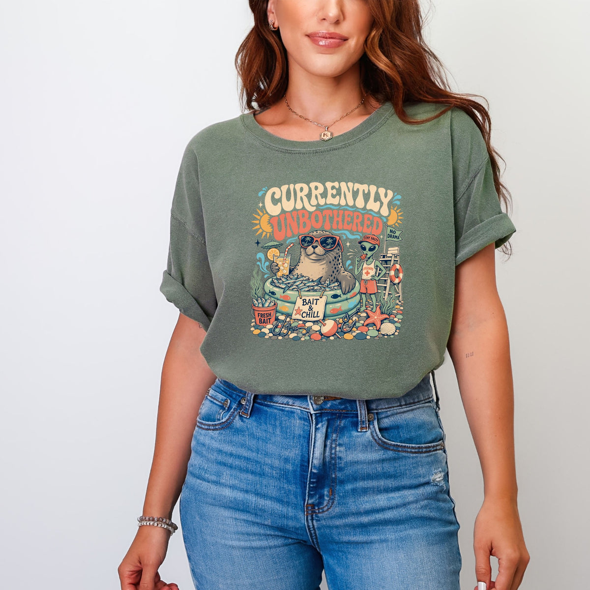 Graphic tee with seal and alien at the beach, text "Currently Unbothered".