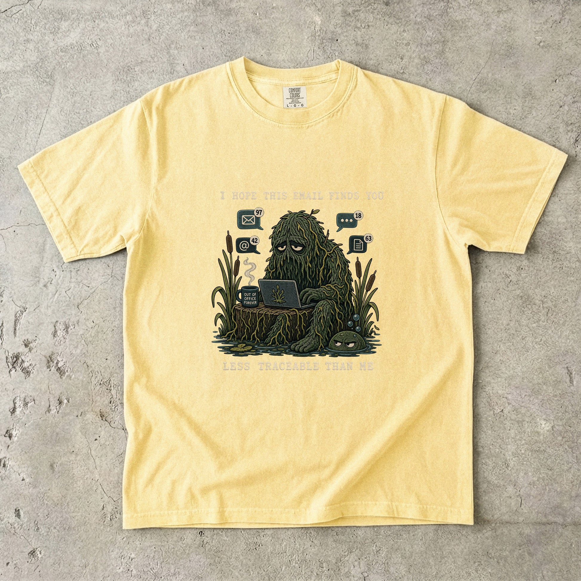 Yellow t-shirt with illustration of a swamp creature at a laptop, "I hope this email finds you" and "Less traceable than me".