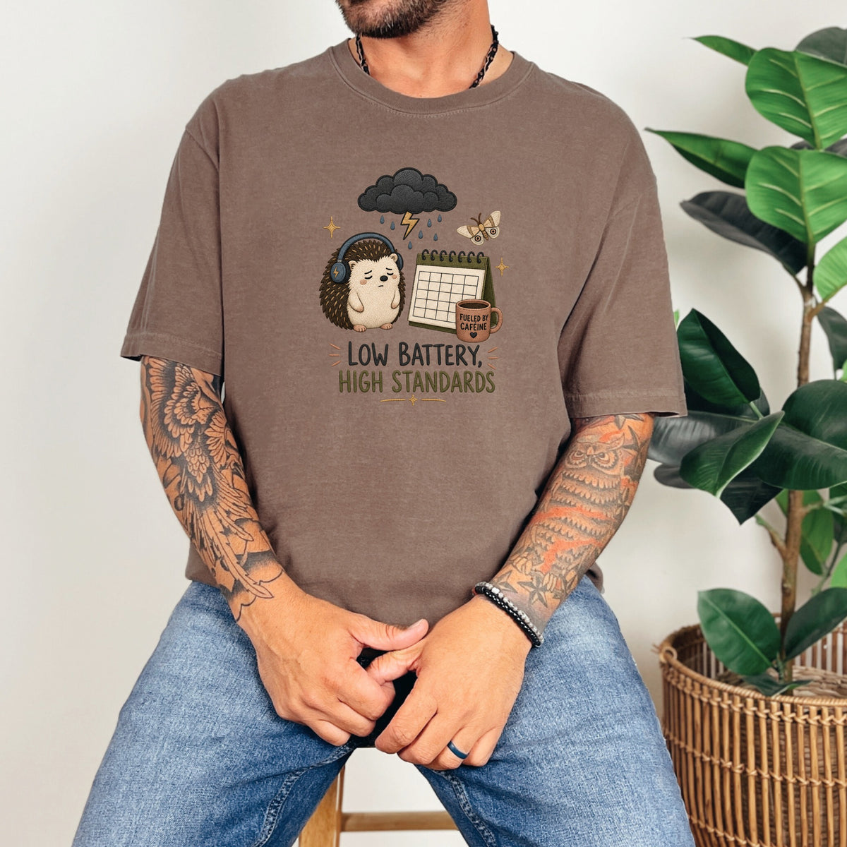 T-shirt graphic with a sad hedgehog, storm cloud, calendar, and text "Low Battery, High Standards."