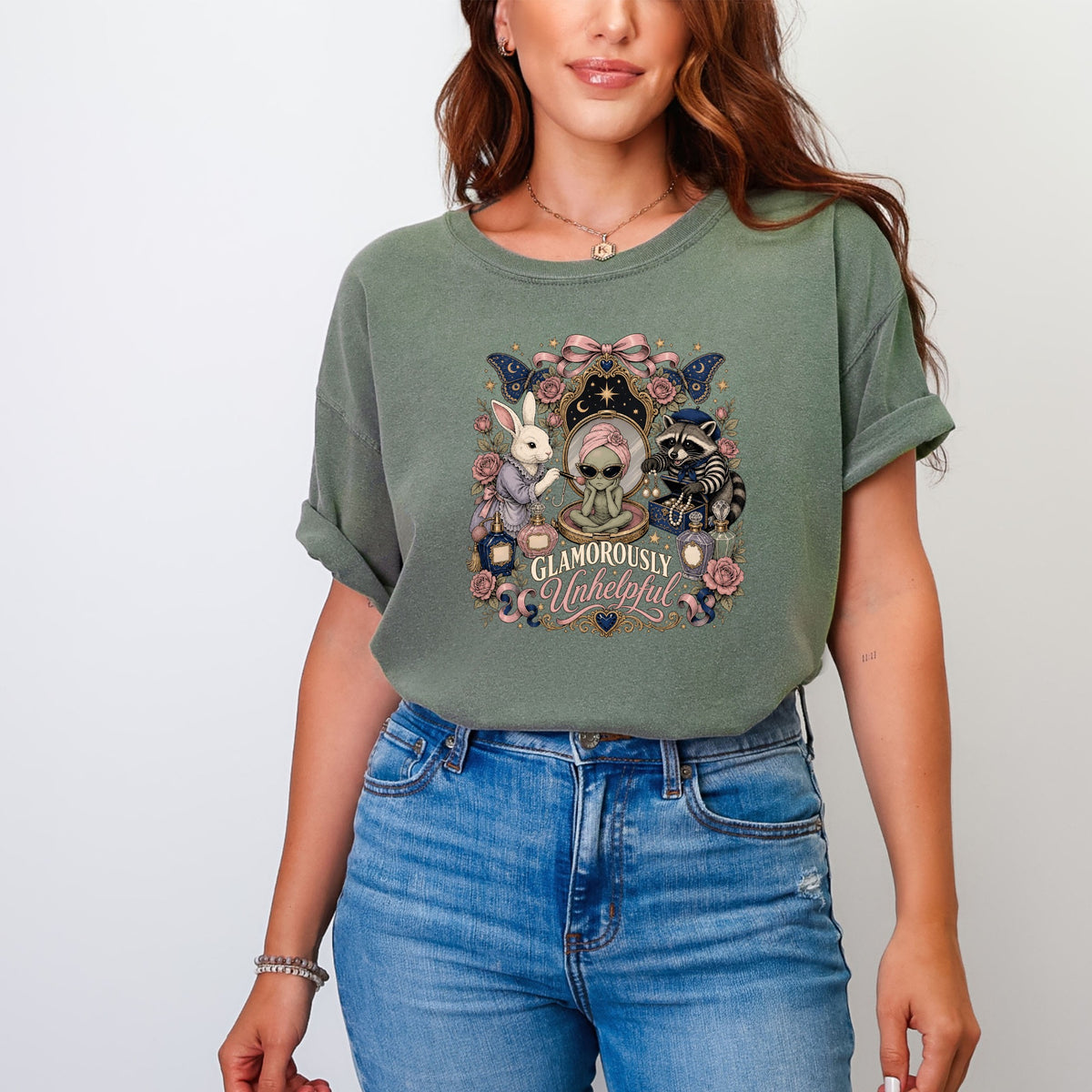 Green t-shirt with whimsical graphic of a rabbit and raccoon around a mirror with text "Glamorously Unhelpful."