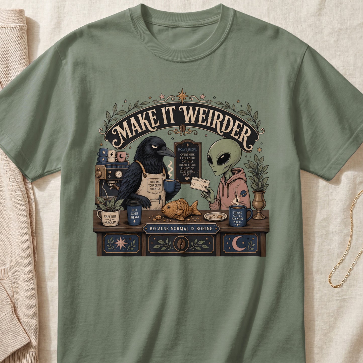 T-shirt graphic: crow and alien at coffee bar, "Make It Weirder" text.