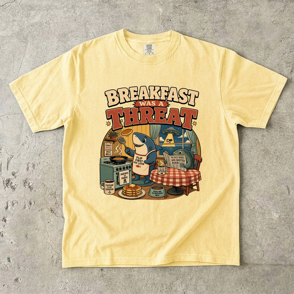 Yellow t-shirt with a cartoon shark cooking breakfast, text reads "Breakfast was a threat".