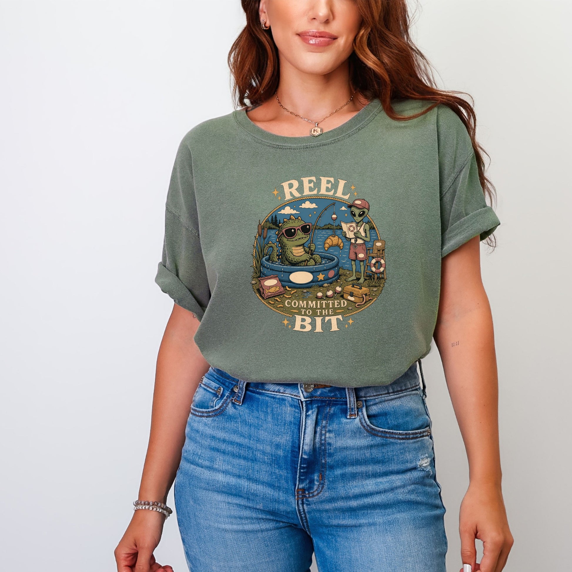 T-shirt with graphic of alien and alligator fishing with text "REEL COMMITTED TO THE BIT."