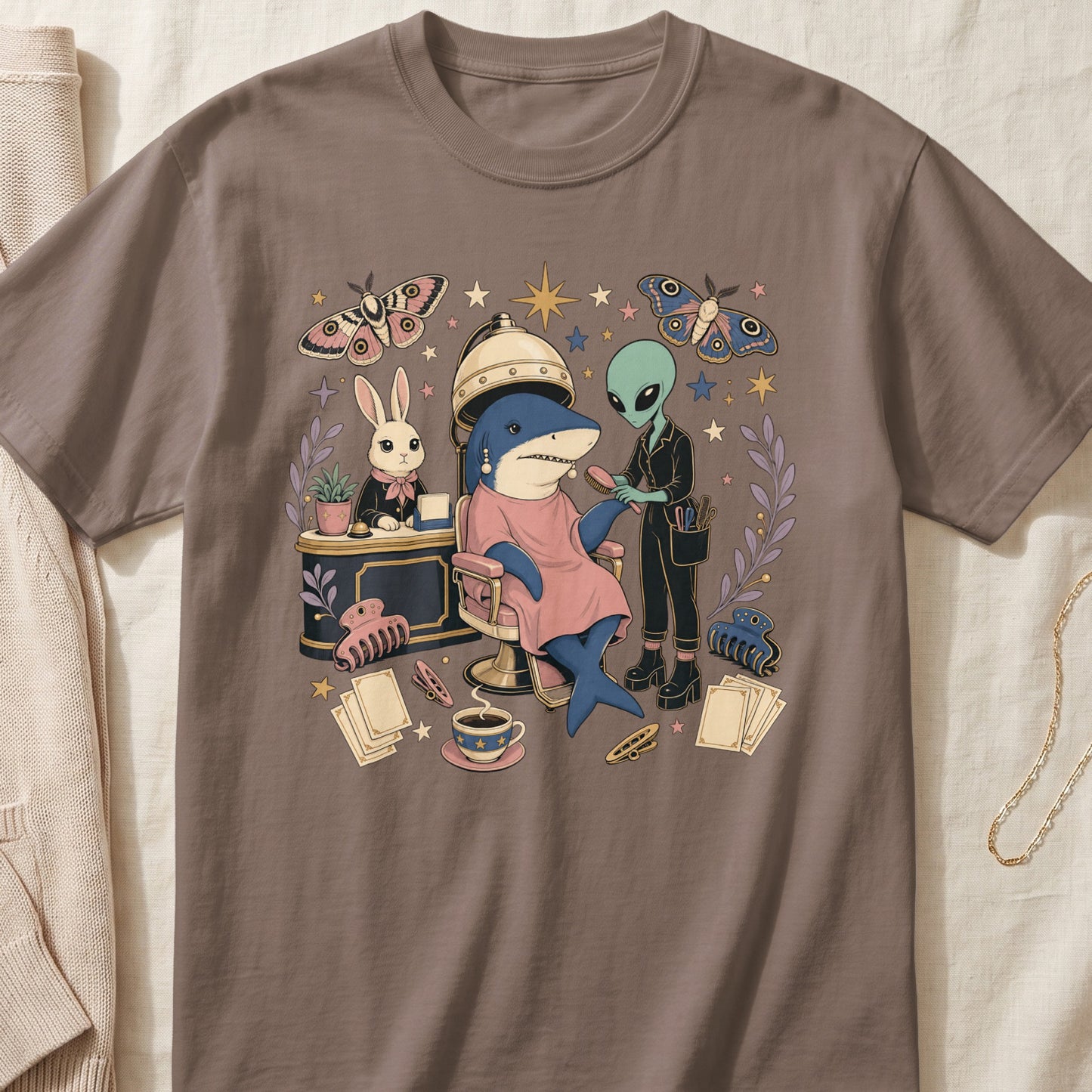 A brown t-shirt featuring an illustration of an alien styling a shark's hair at a salon.