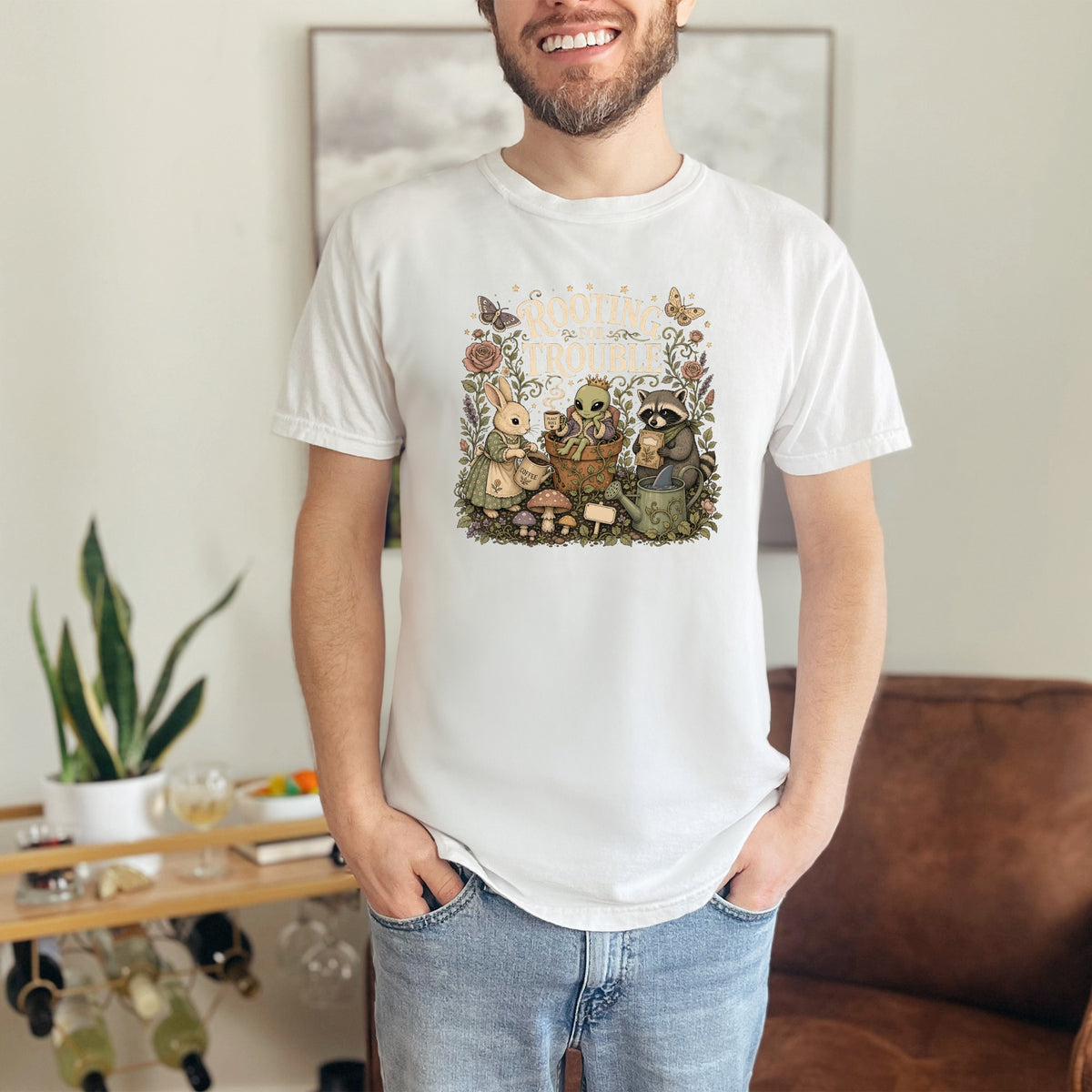 White t-shirt with "Rooting For Trouble" text and illustration of rabbit, alien, and raccoon.