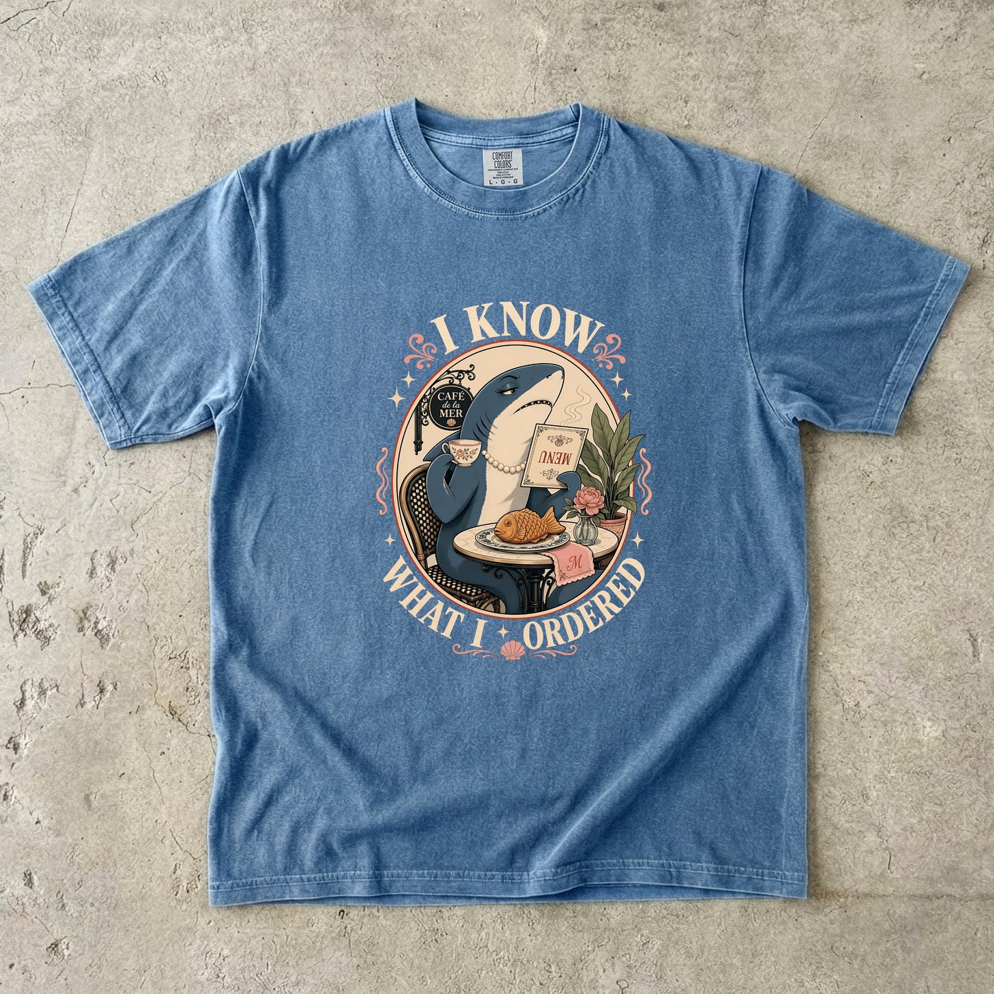 Blue t-shirt with a shark at a cafe table, holding a menu and coffee, text "I KNOW WHAT I ORDERED".