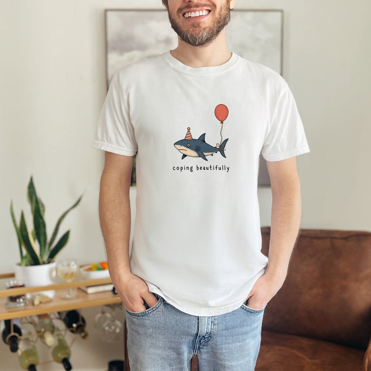 White t-shirt with a cartoon shark wearing a party hat and holding a balloon.
