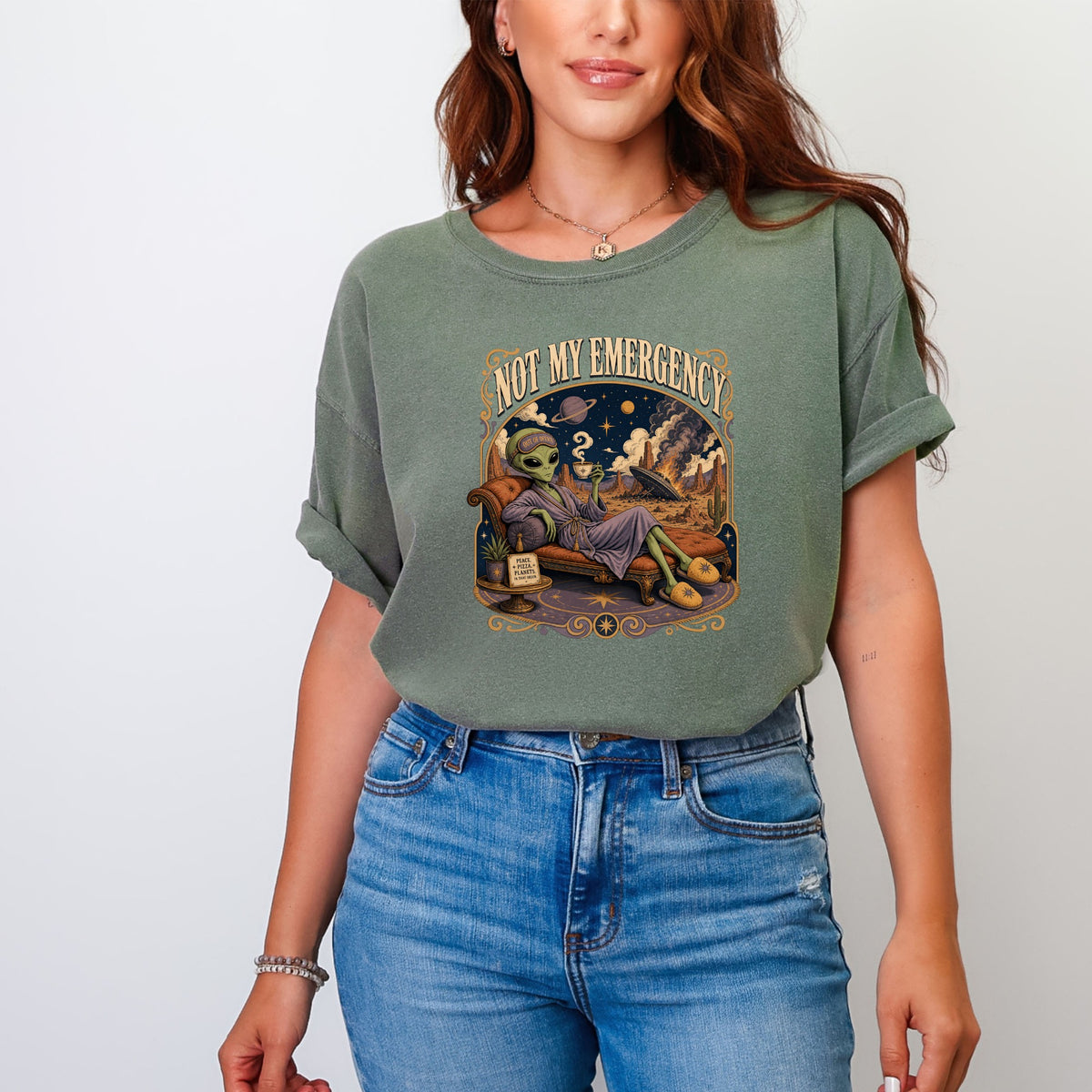 T-shirt graphic with alien relaxing, "Not My Emergency" text, and desert landscape.