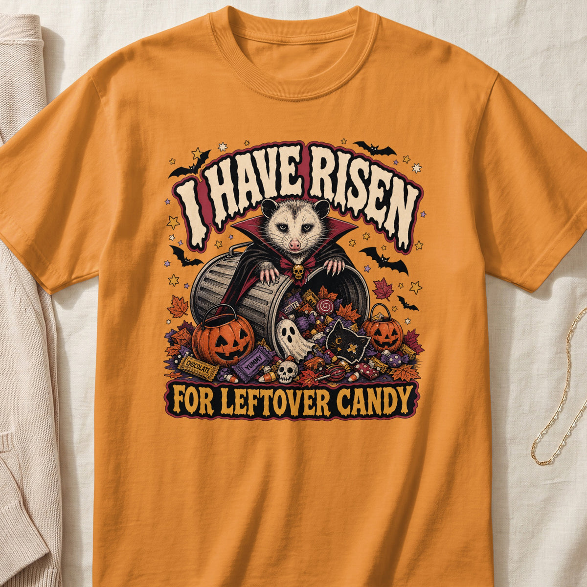 Orange t-shirt with a Halloween design featuring a vampire possum and candy, reading "I HAVE RISEN FOR LEFTOVER CANDY."