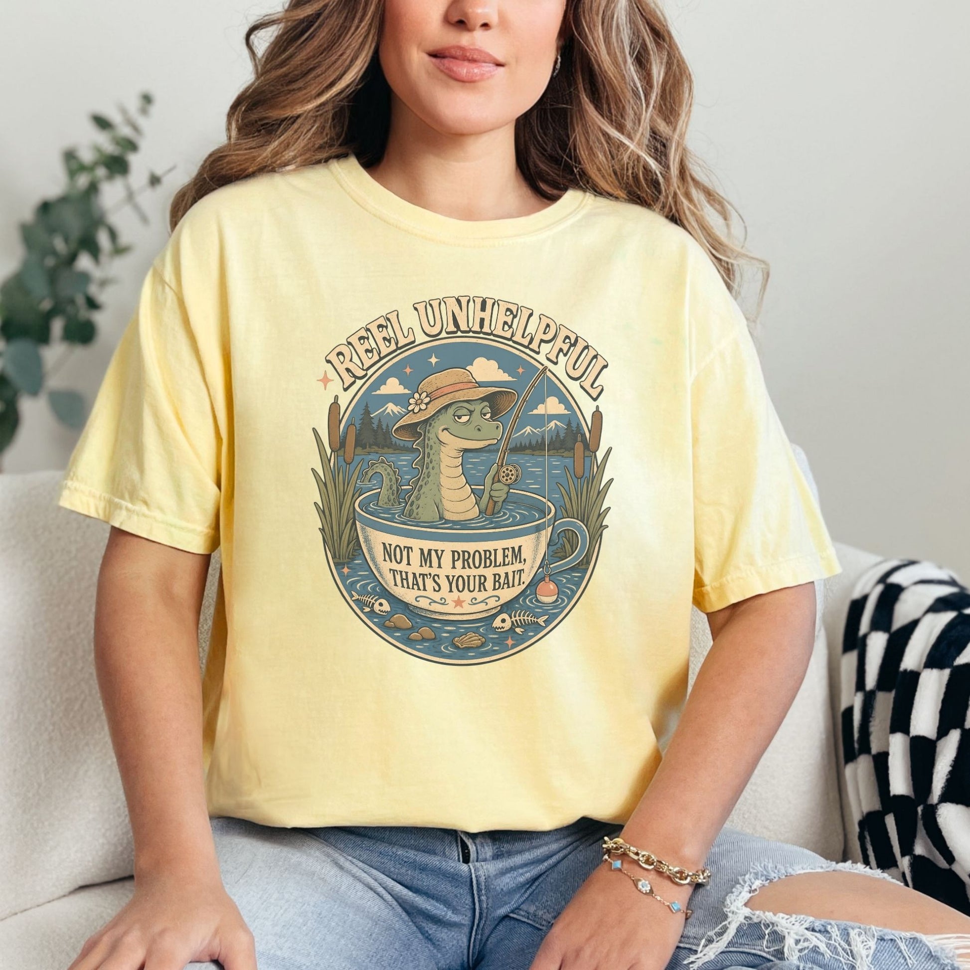Yellow t-shirt with graphic of alligator fishing in a teacup, text "Reel Unhelpful".