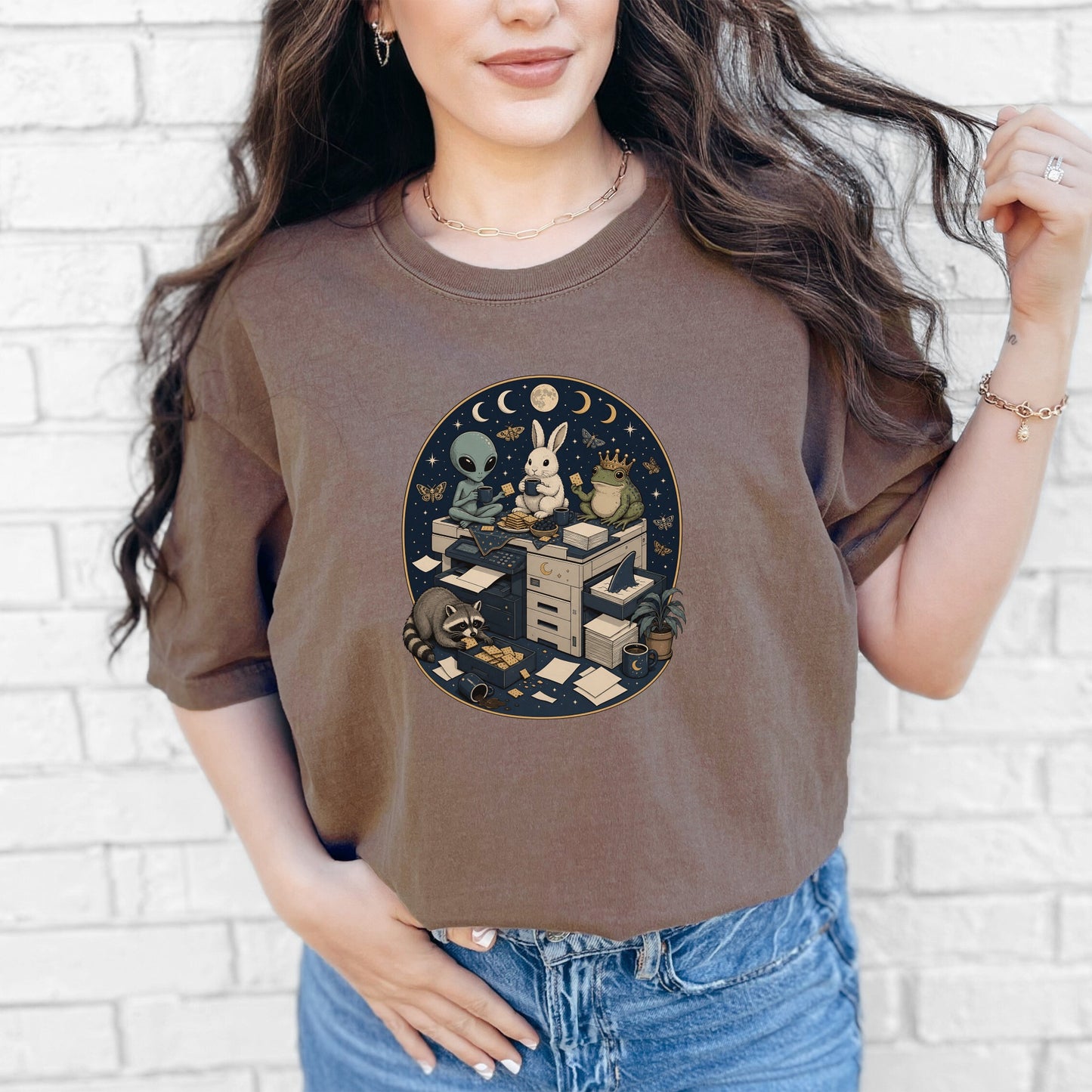 A woman wearing a brown t-shirt featuring an oval graphic of animals and an alien around office equipment.