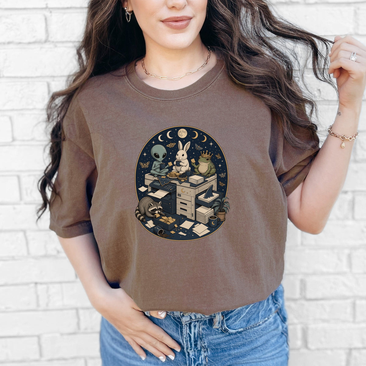 A woman wearing a brown t-shirt featuring an oval graphic of animals and an alien around office equipment.
