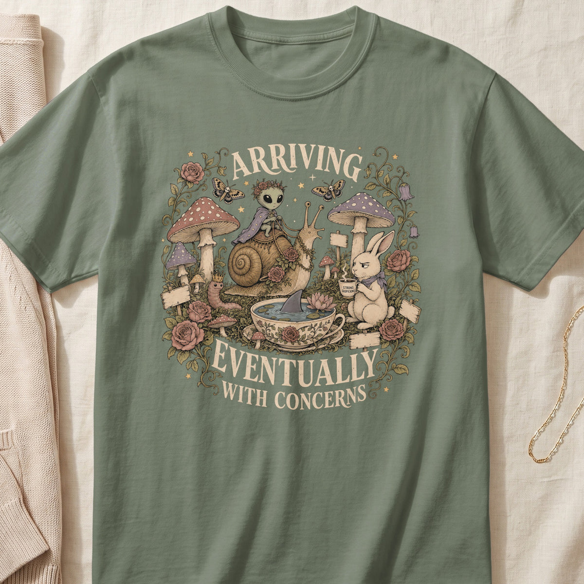 Green t-shirt with a detailed whimsical graphic featuring an alien on a snail, a rabbit, mushrooms, and text.