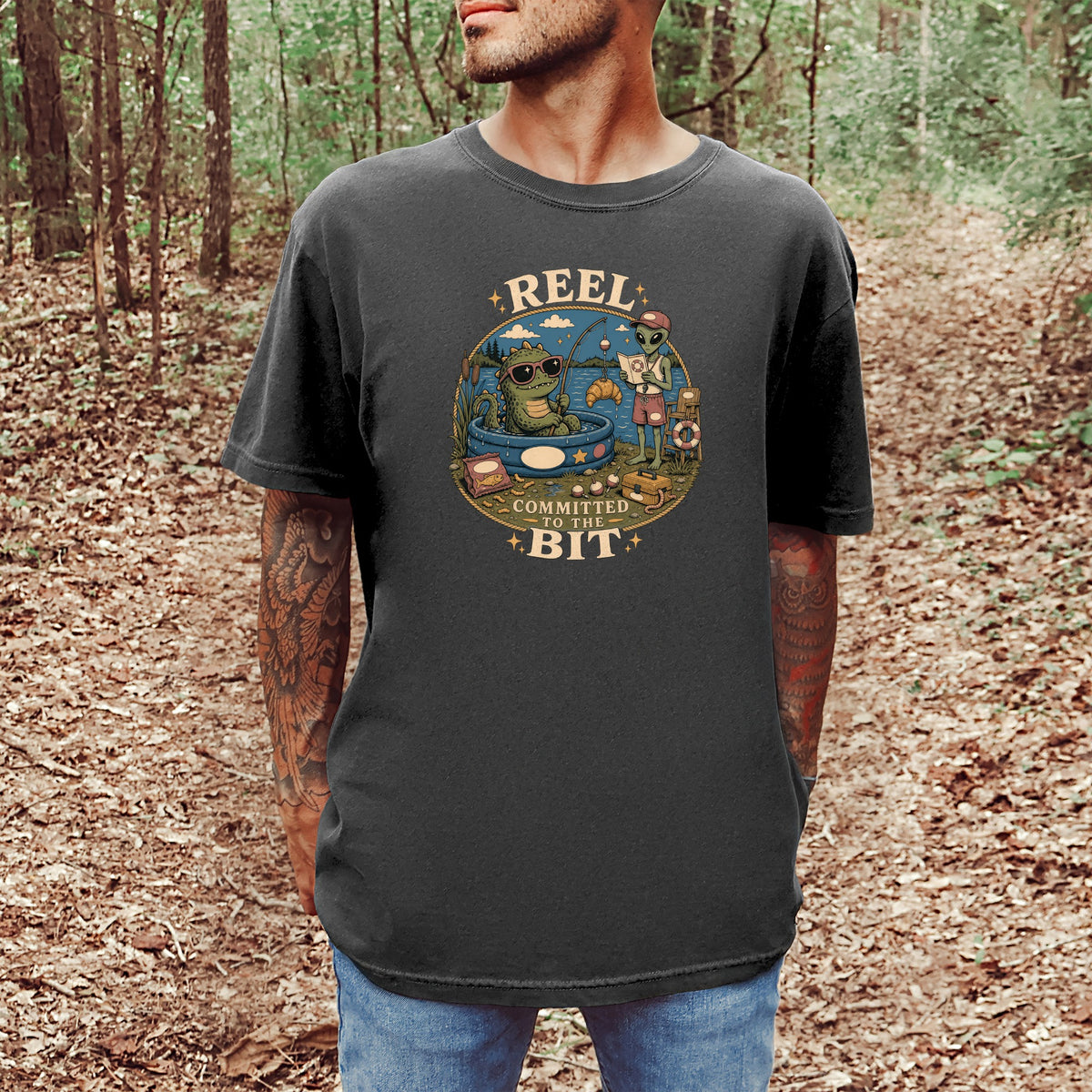 T-shirt graphic: a dragon and alien fishing, text reads "REEL COMMITTED TO THE BIT"