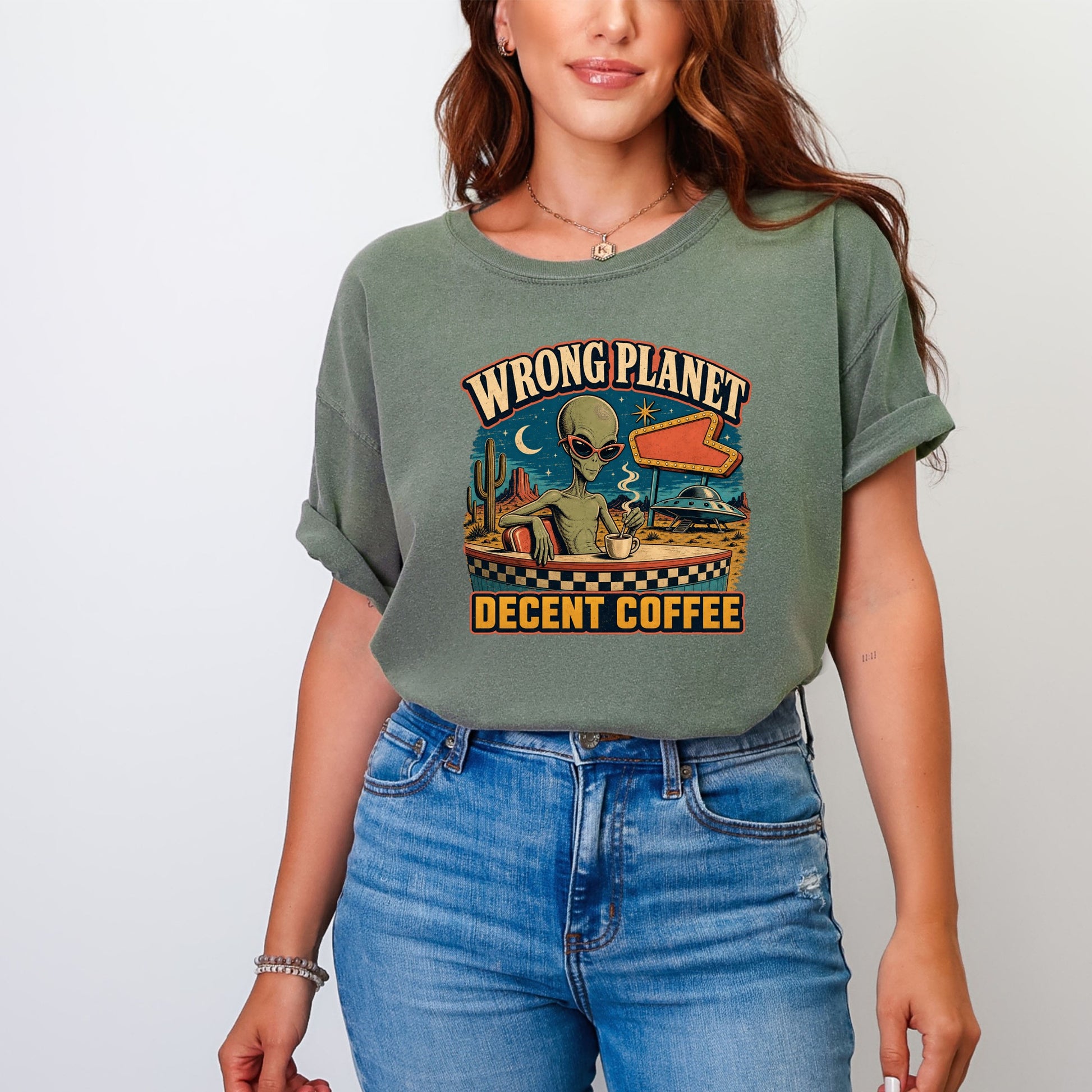 Green t-shirt with alien sitting at a counter drinking coffee, text "Wrong Planet Decent Coffee."