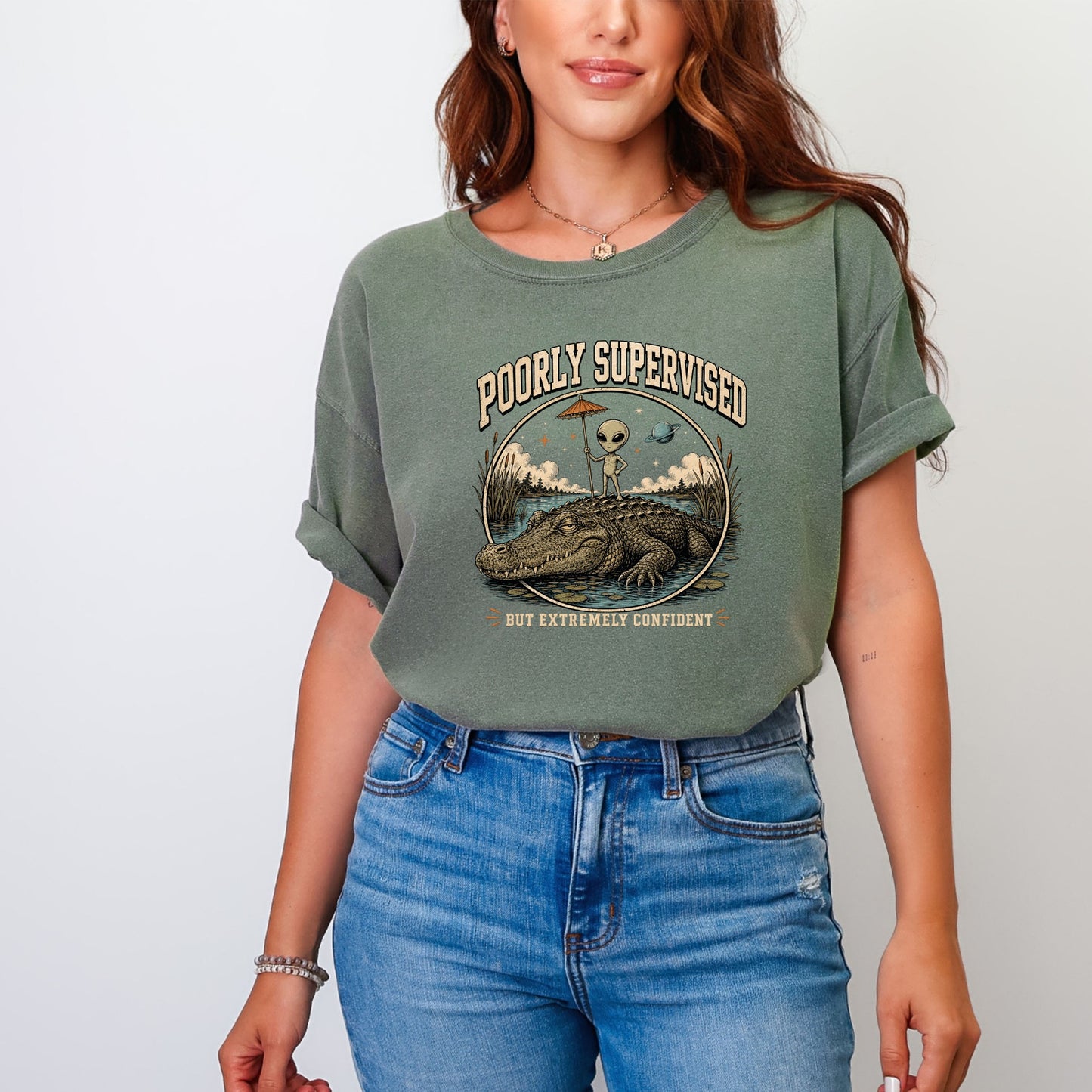 T-shirt graphic with alien on alligator, reading "Poorly Supervised But Extremely Confident".