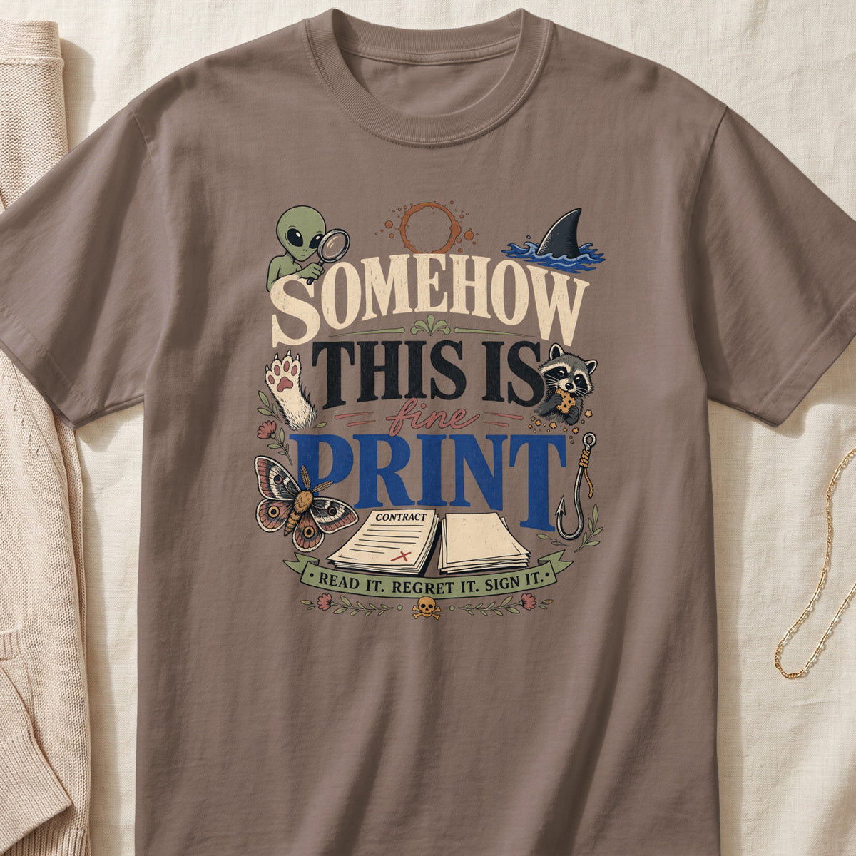 Brown crewneck t-shirt featuring a colorful graphic with text reading SOMEHOW THIS IS FINE PRINT.