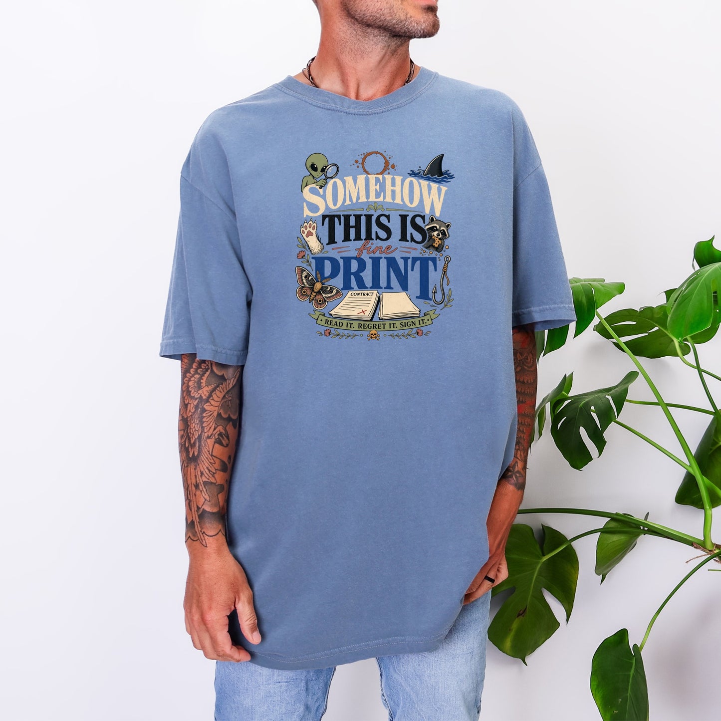 A man wearing an oversized blue t-shirt featuring graphic text and illustrations.