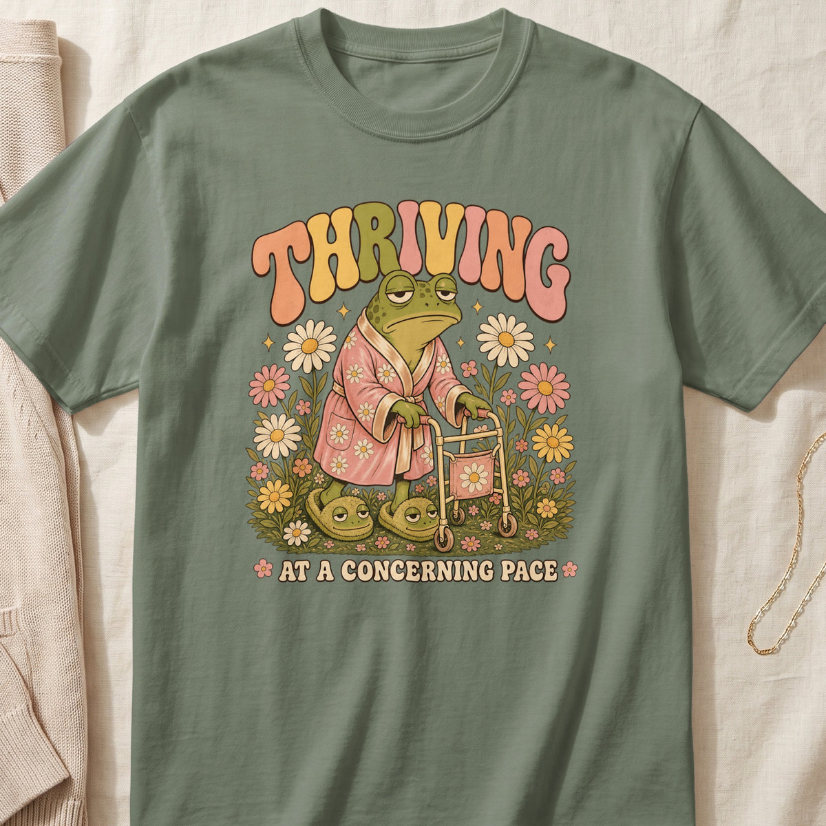 A frog in a bathrobe and slippers uses a walker with "THRIVING AT A CONCERNING PACE" text.