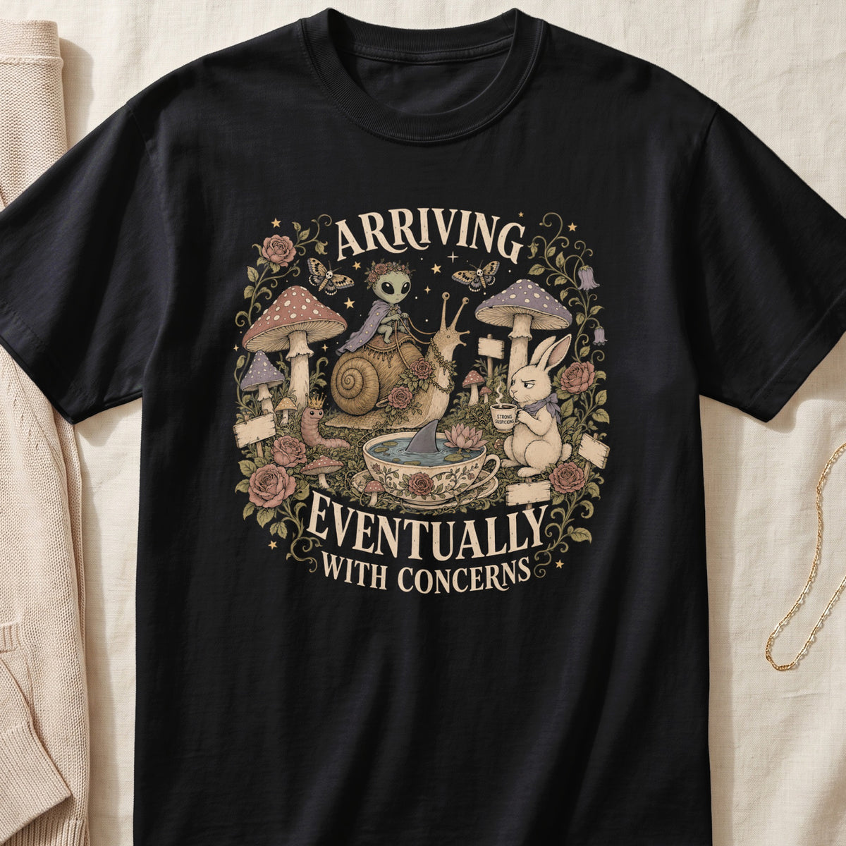 Black t-shirt with "Arriving Eventually With Concerns" text and whimsical forest graphic.